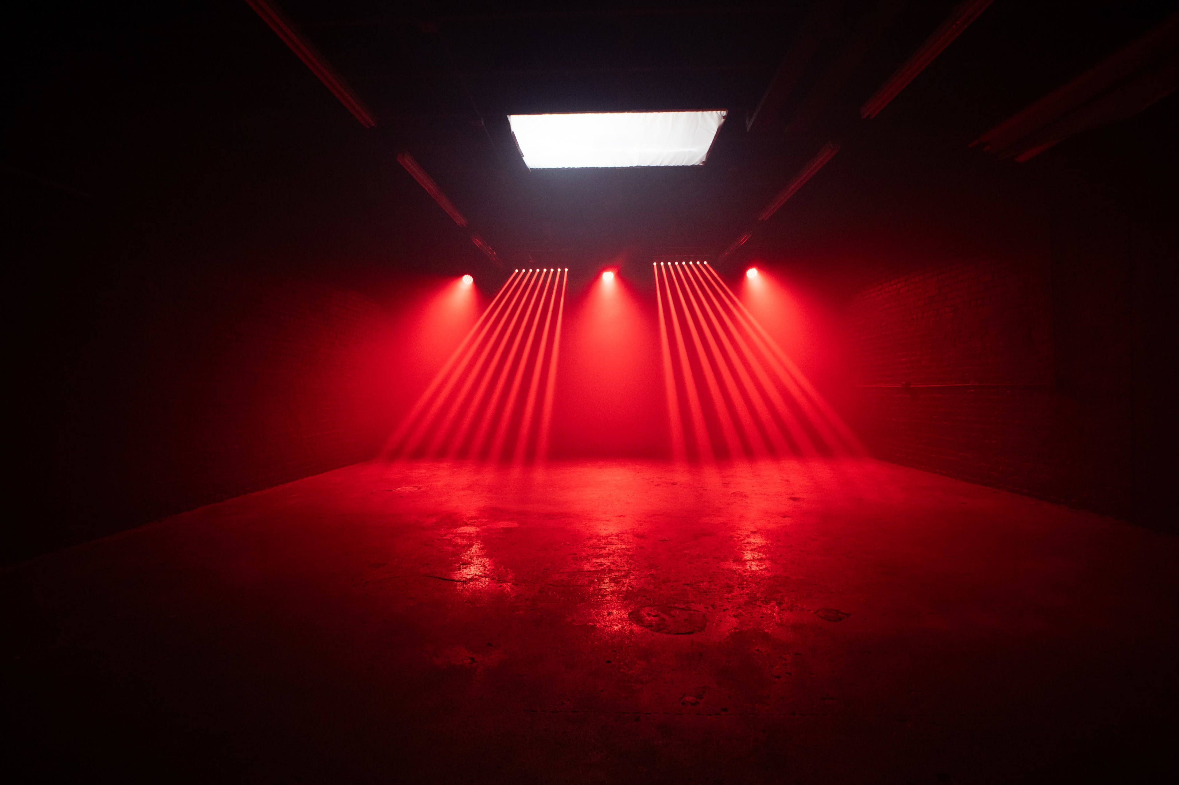 A dimly lit room features red light beams illuminating the space from above, creating a dramatic atmosphere.