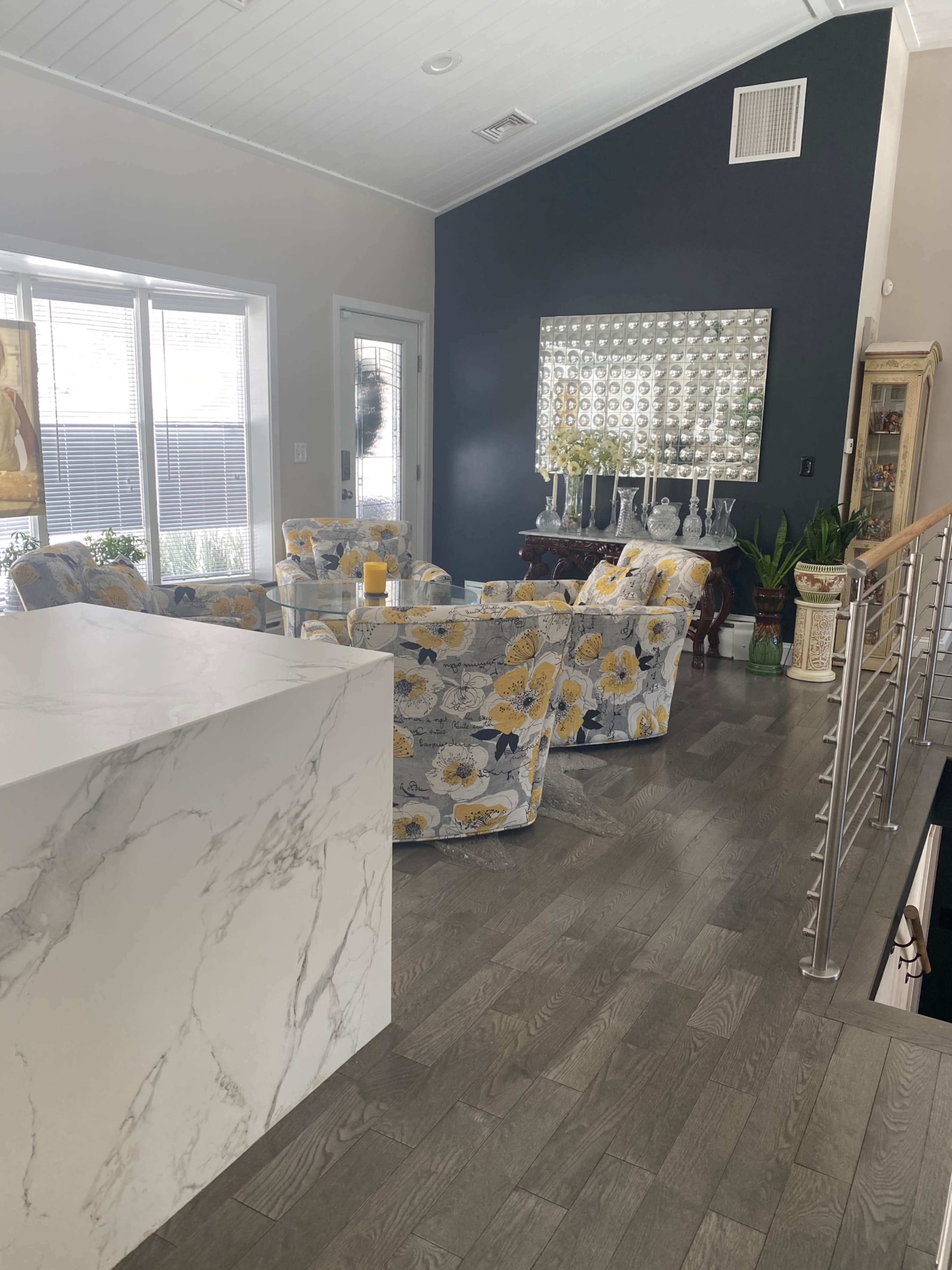 A living room with floral-patterned chairs, a marble kitchen island, and decorative mirrors on a dark wall.