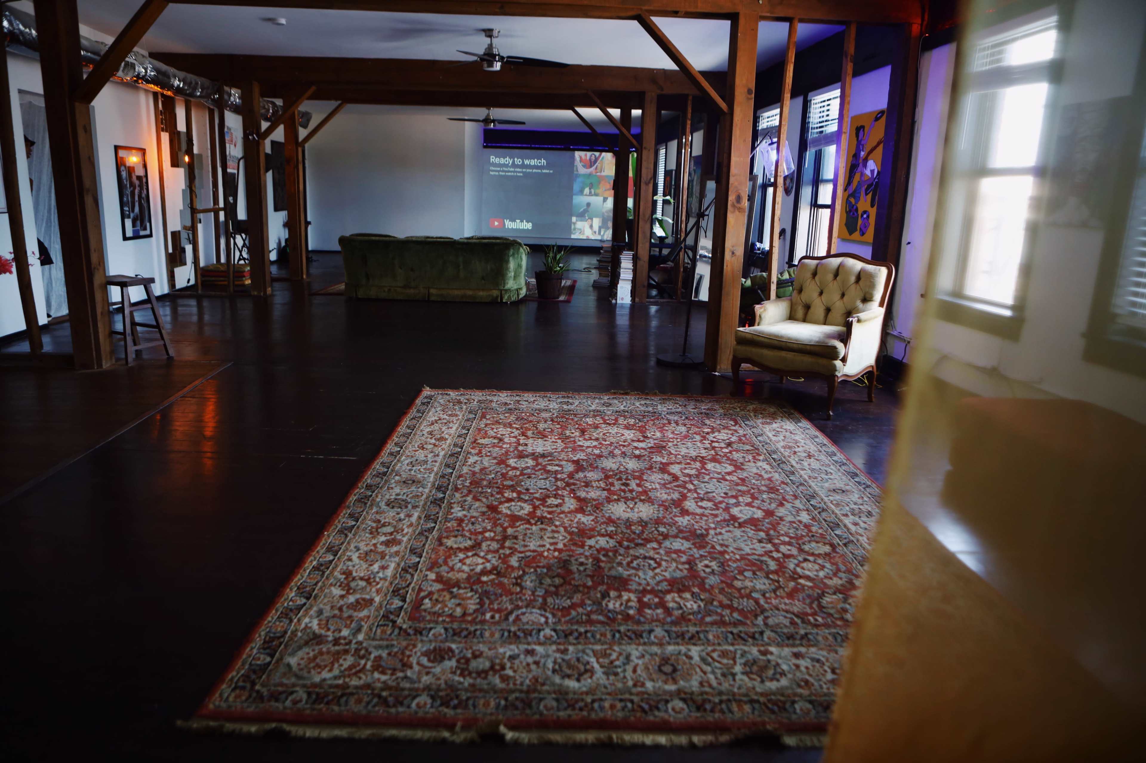 A spacious room with a green couch, a vintage armchair, and a large screen displaying a video.