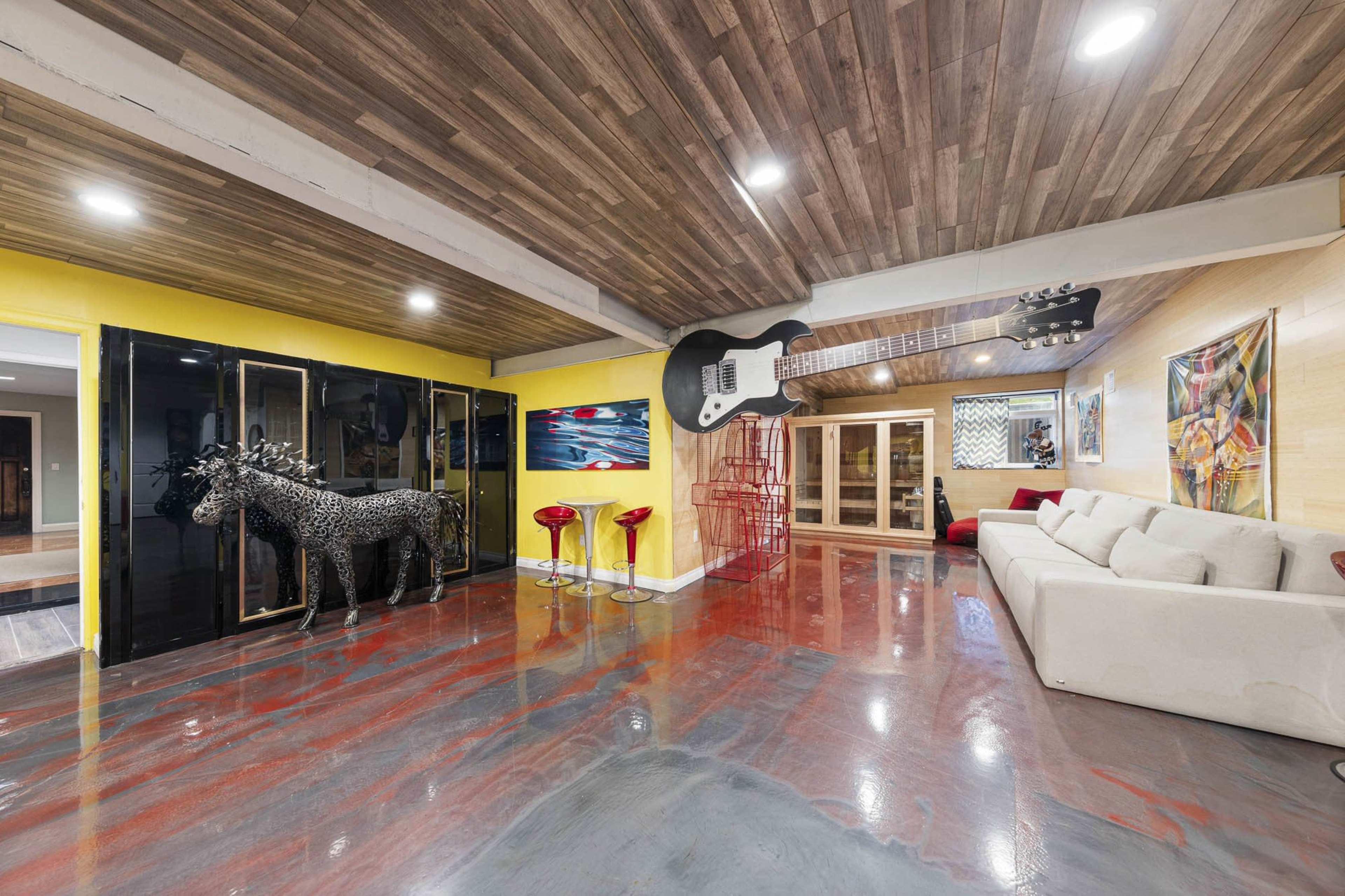 A spacious interior features a yellow wall, wooden ceiling, modern furniture, and eclectic art pieces, including a large guitar sculpture and a decorative horse figure.