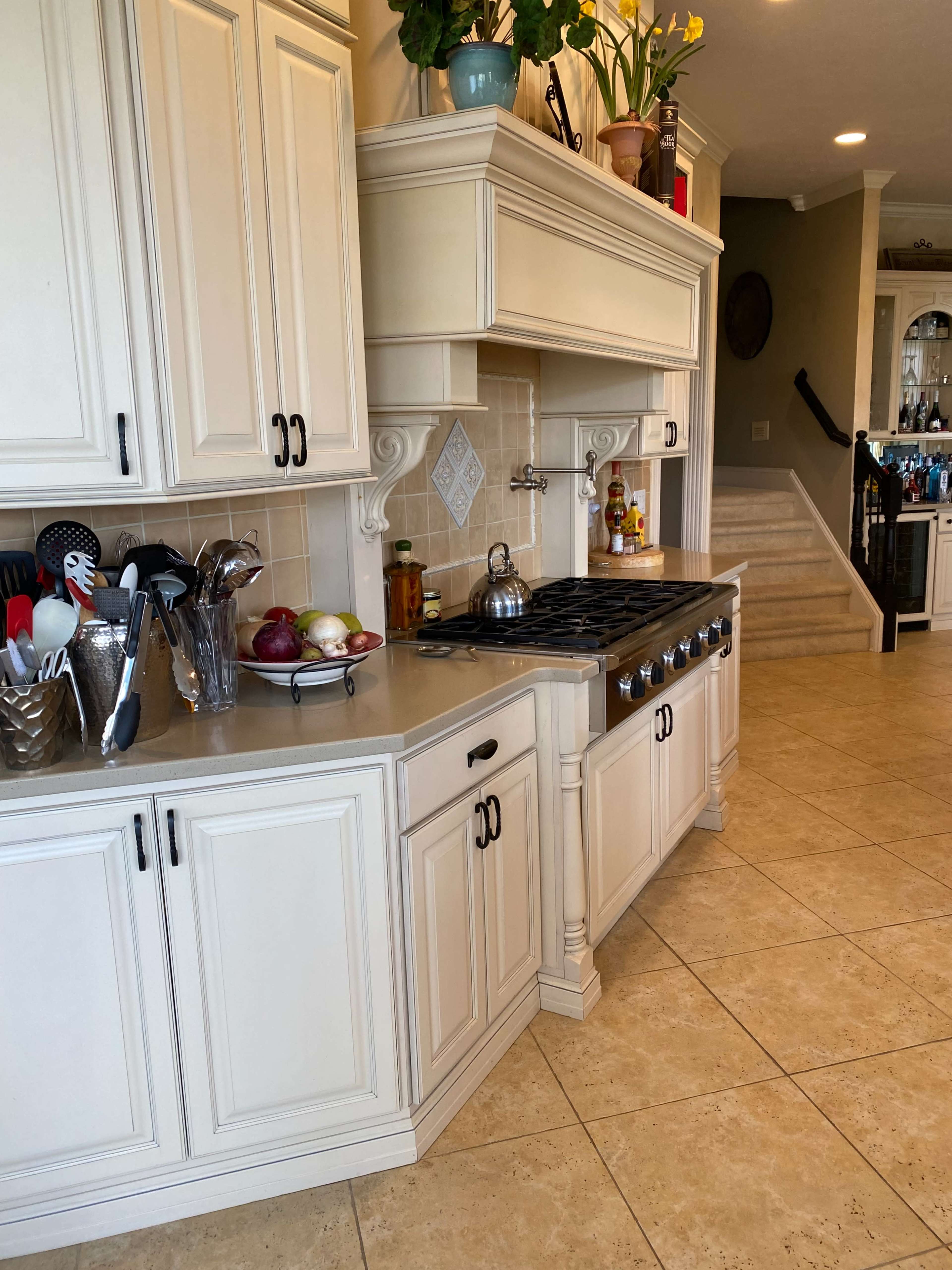 A spacious kitchen featuring light-colored cabinetry, a large gas stove, and various utensils arranged on the countertop.