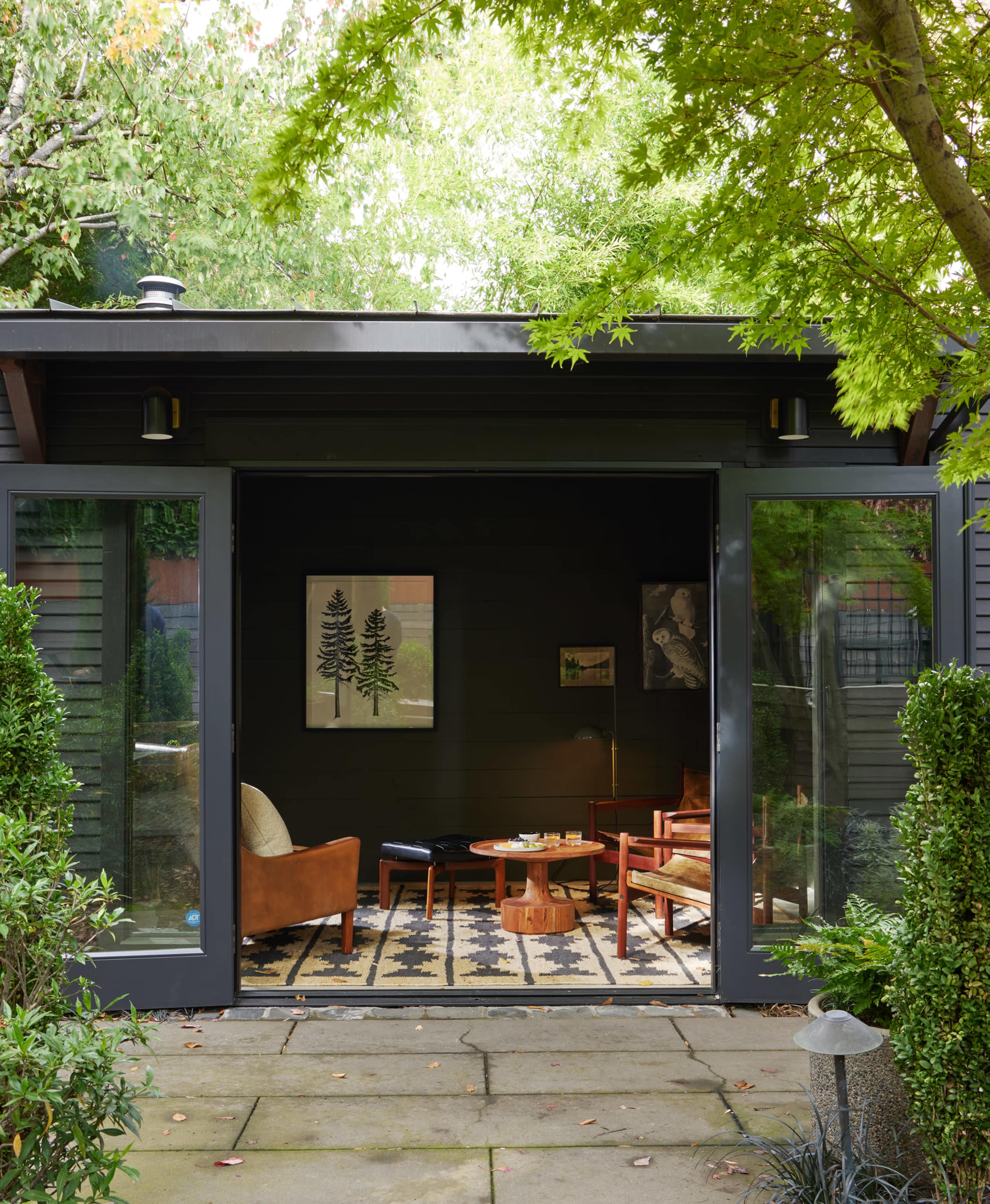 A modern, open living space with large glass doors leads into a garden surrounded by greenery.