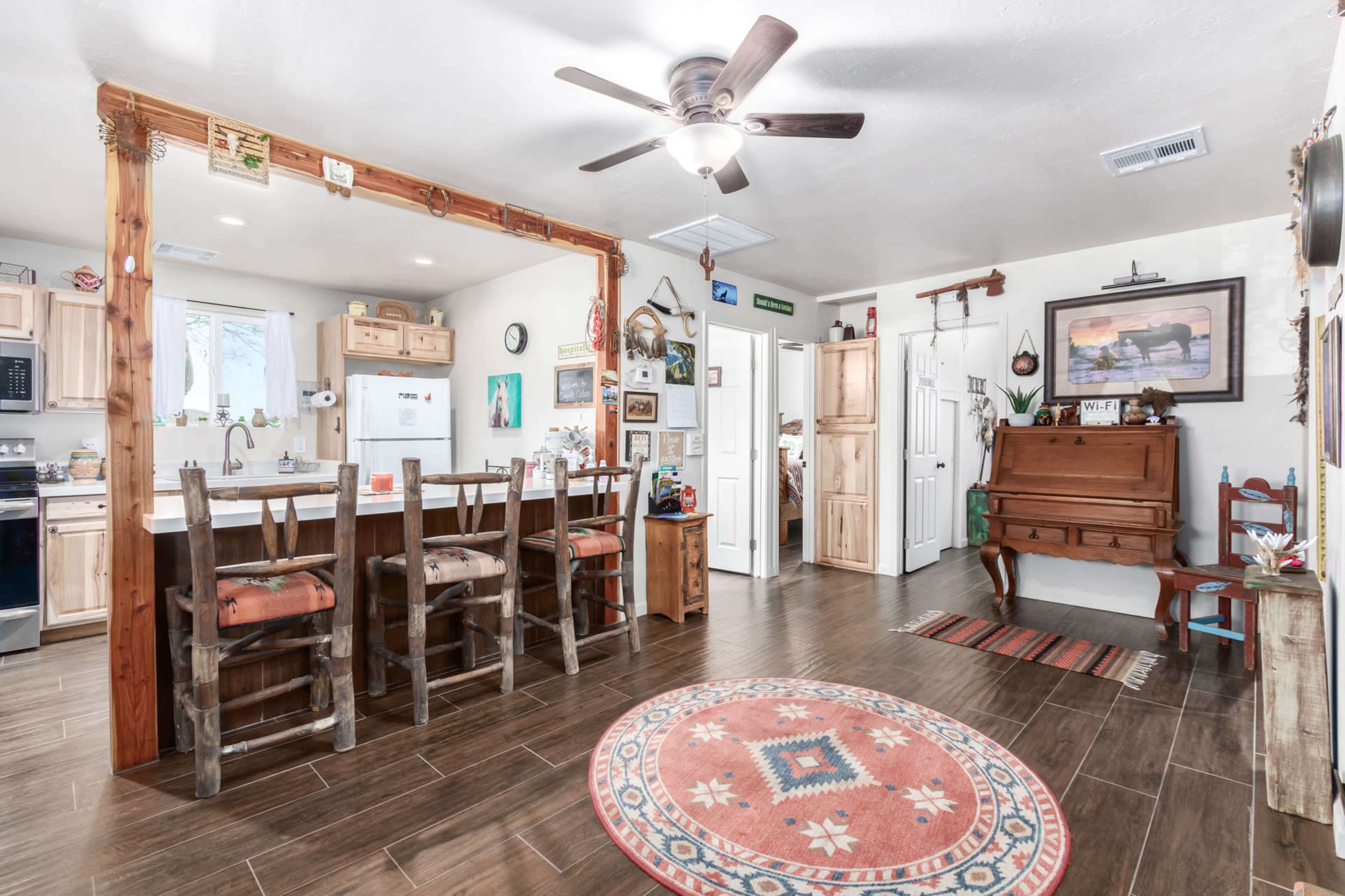A cozy interior space featuring a kitchen area with wooden bar stools, a dining area with a round rug, and a partitioned living area decorated with various artwork and furnishings.