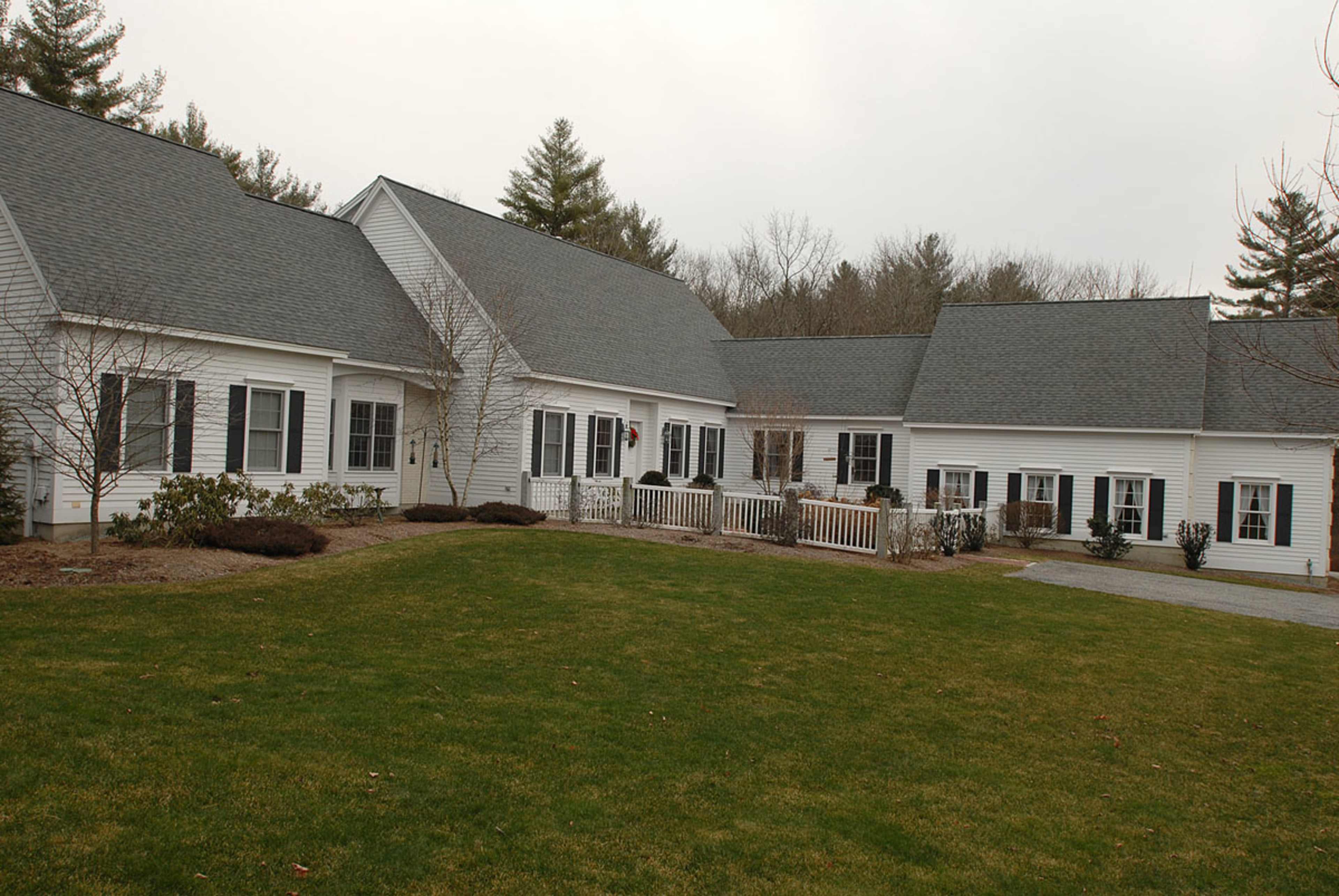 The image shows a large white house with multiple sections and a well-maintained lawn, surrounded by trees.