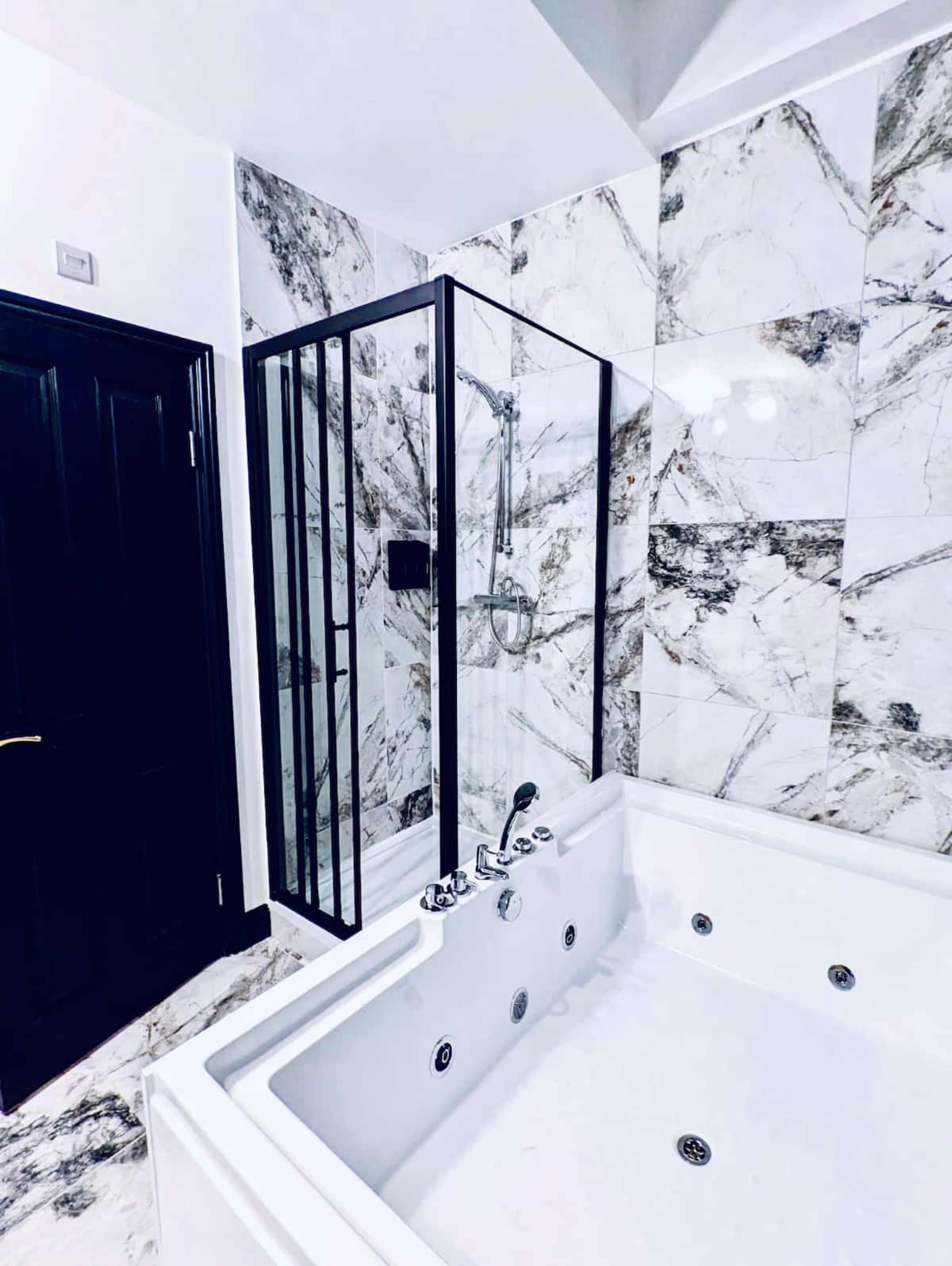 A modern bathroom featuring a glass shower enclosure and a white jacuzzi tub against marble-patterned tiles.