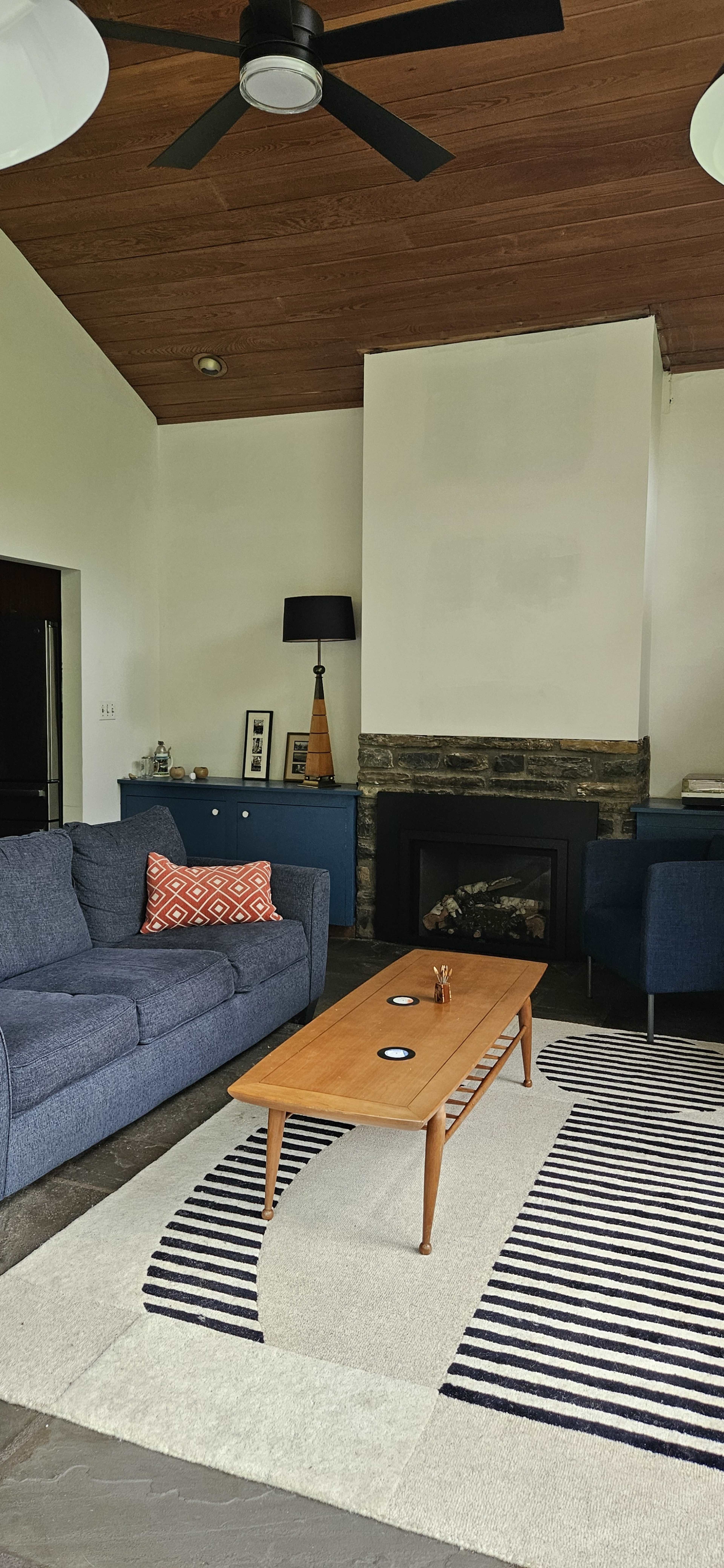 The image shows a modern living room featuring a blue couch, a wooden coffee table, and a cozy fireplace against a stone wall.