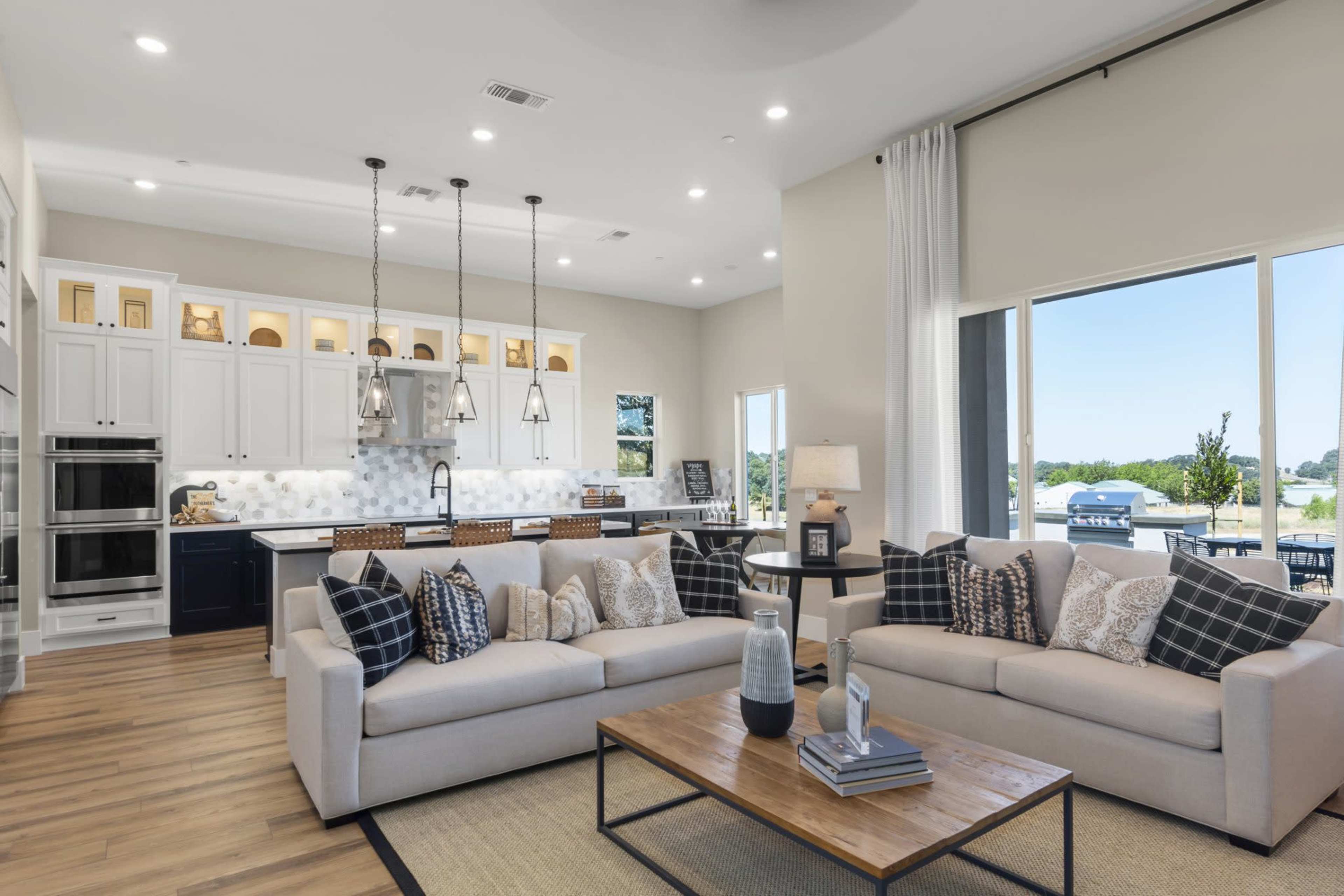 The image shows a modern living room with two sofas, a coffee table, and a view of a kitchen area in the background.