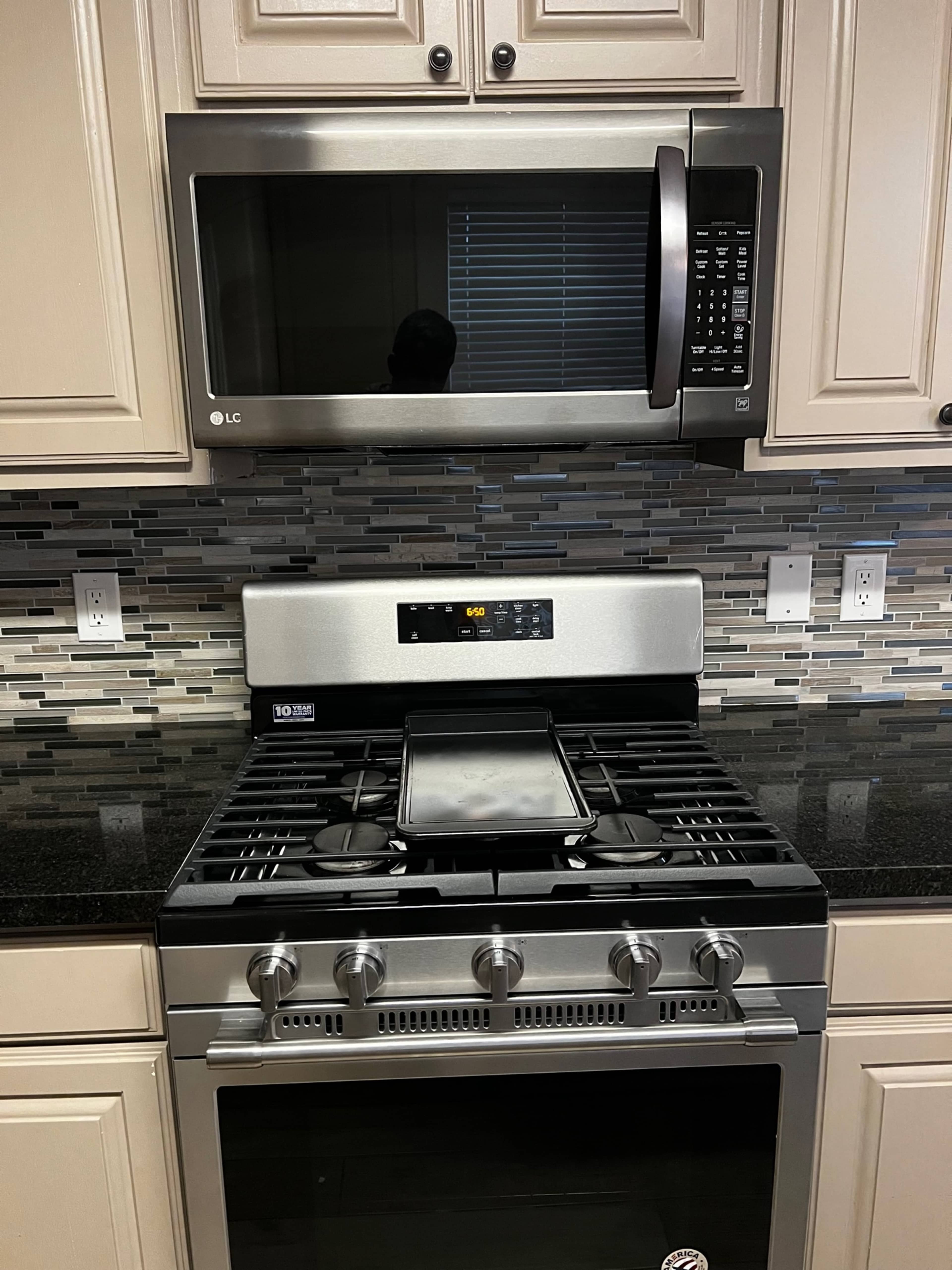 A kitchen setup featuring a stainless steel microwave above a gas range with a black countertop and a tiled backsplash.