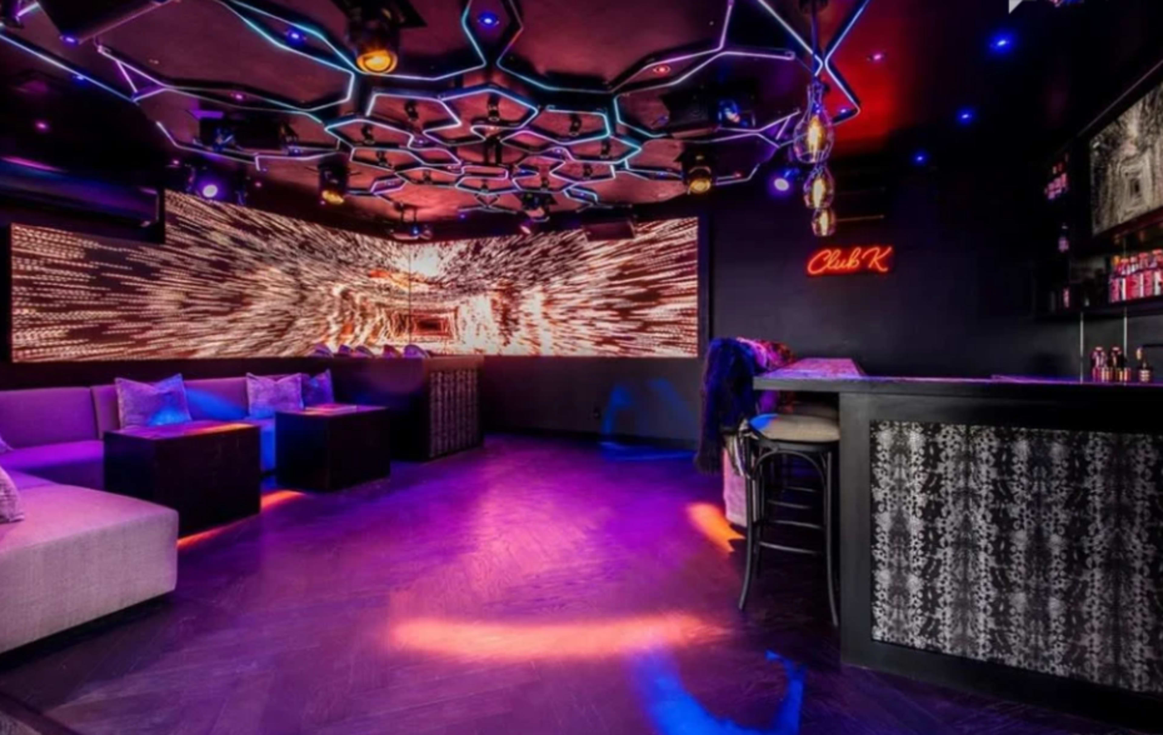 A modern lounge with a bar area and illuminated walls featuring a vibrant visual display, surrounded by seating.
