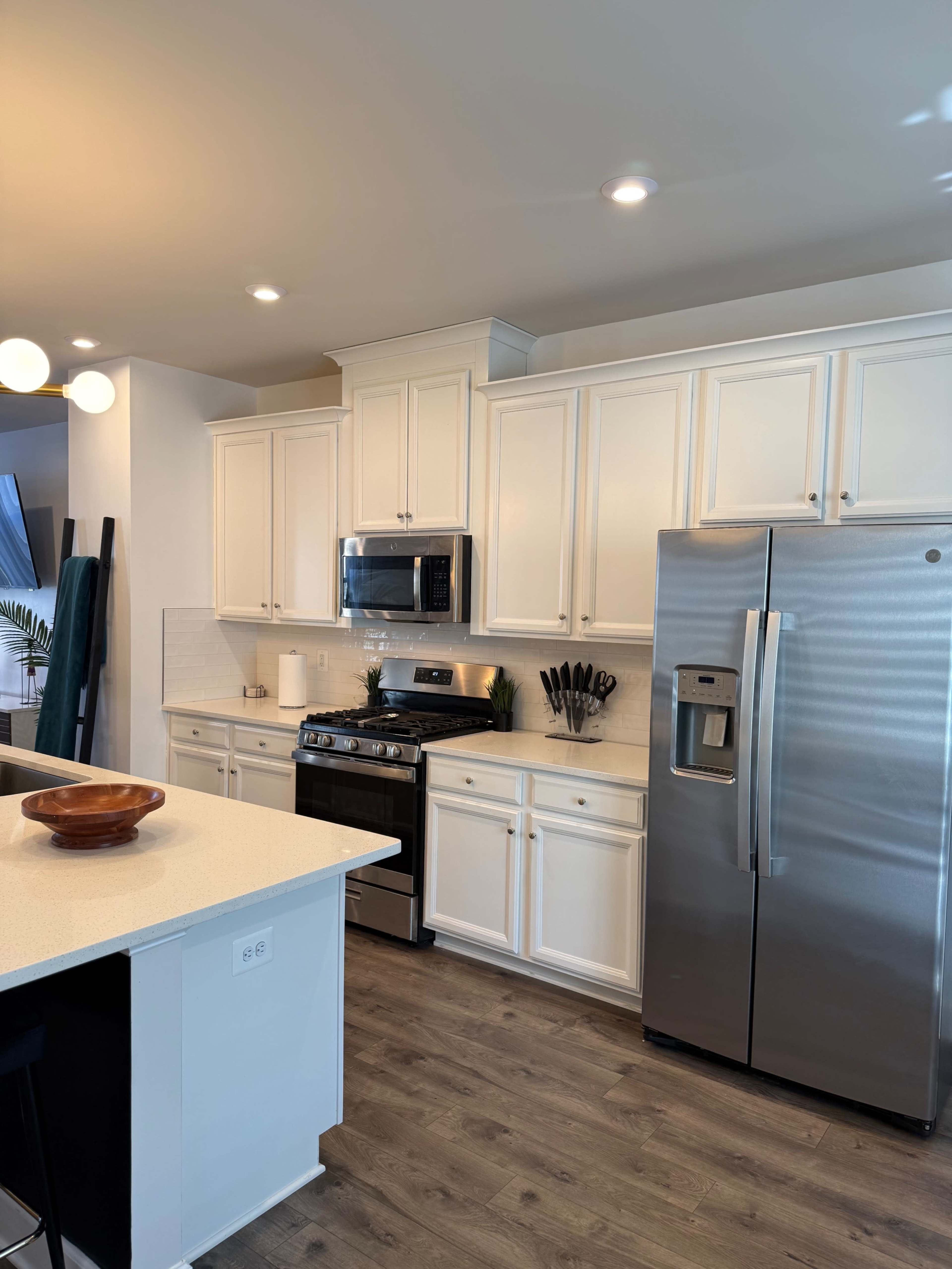 The image shows a modern kitchen with white cabinetry, stainless steel appliances, and a light-colored countertop.