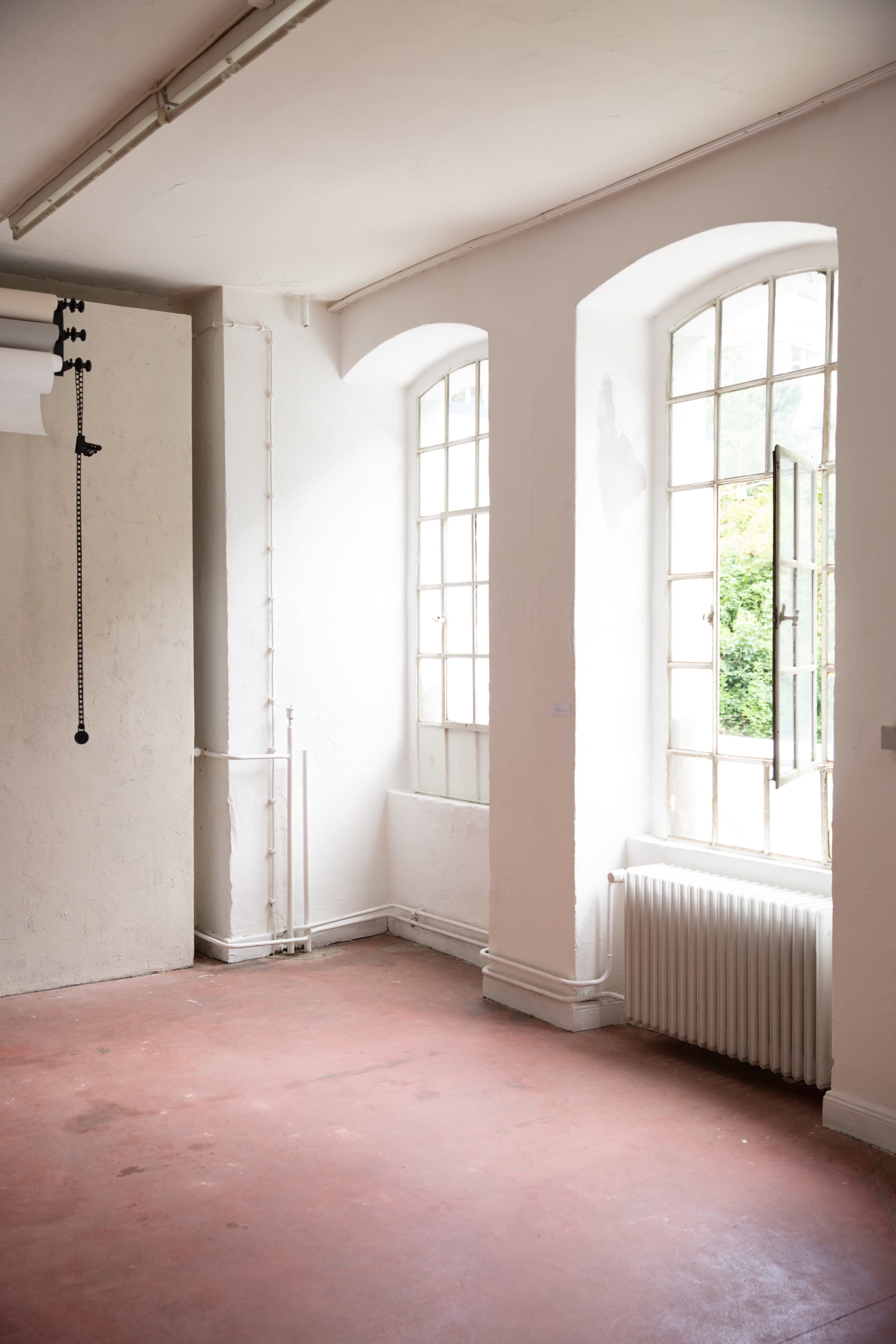 The image shows a minimalistic, empty room with two large windows and a radiator along one wall.