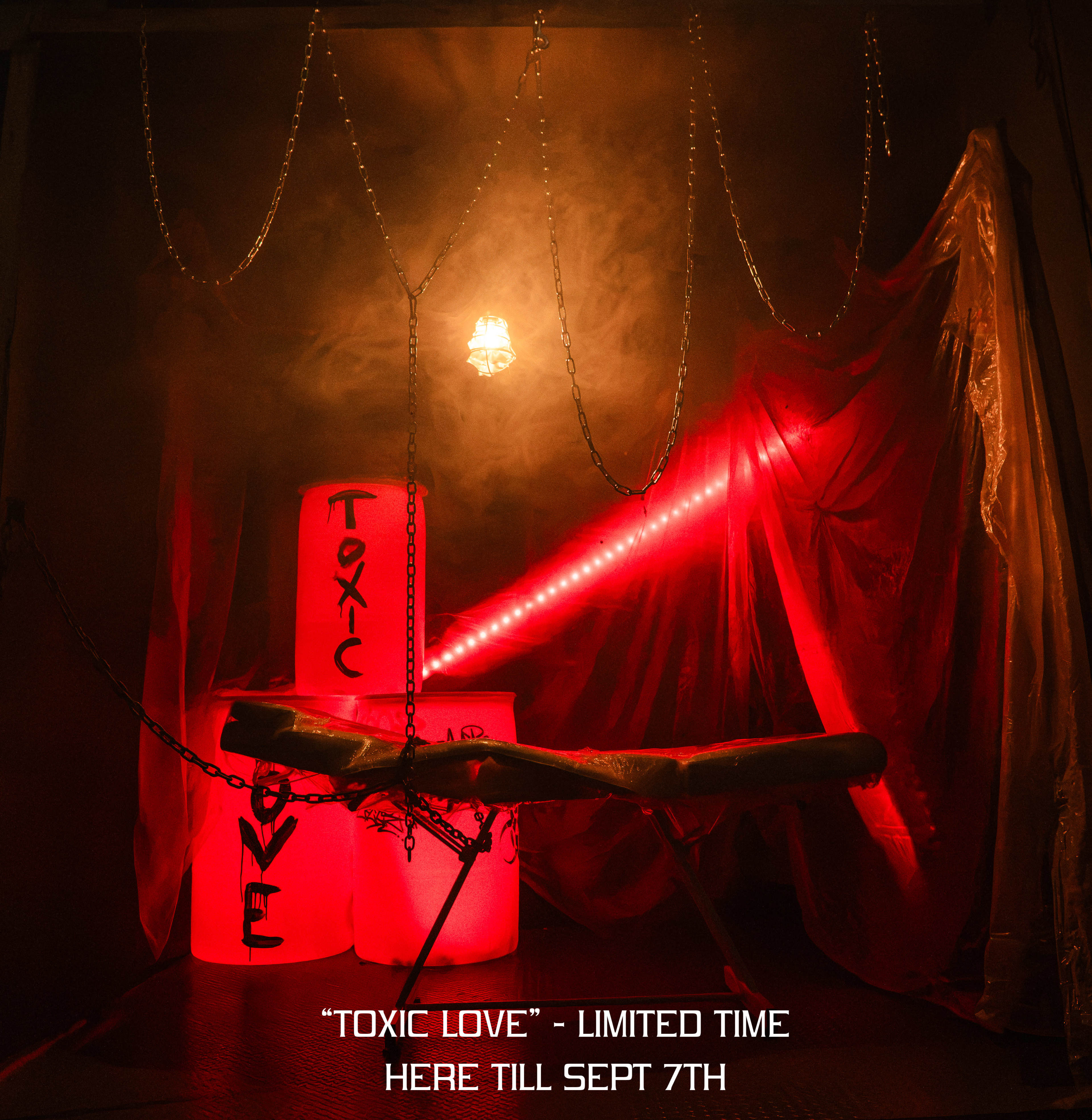The image features a dimly lit, smoky room with red lighting, showcasing barrels labeled "TOXIC LOVE" and a chain-linked bench in front of them.