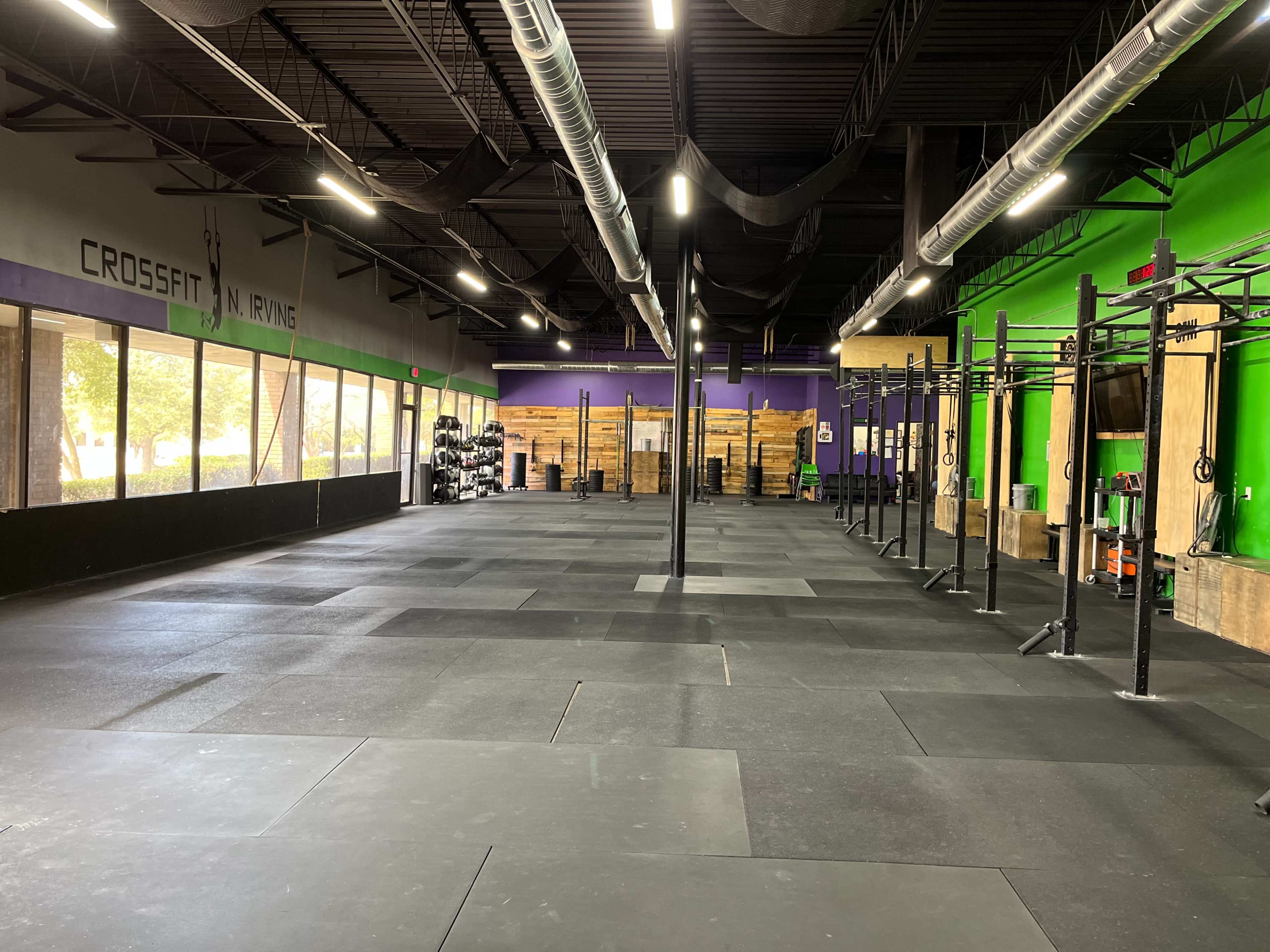 The interior of a CrossFit training facility features a spacious, open floor with rubber flooring, exposed wooden racks, and exercise equipment along the walls.