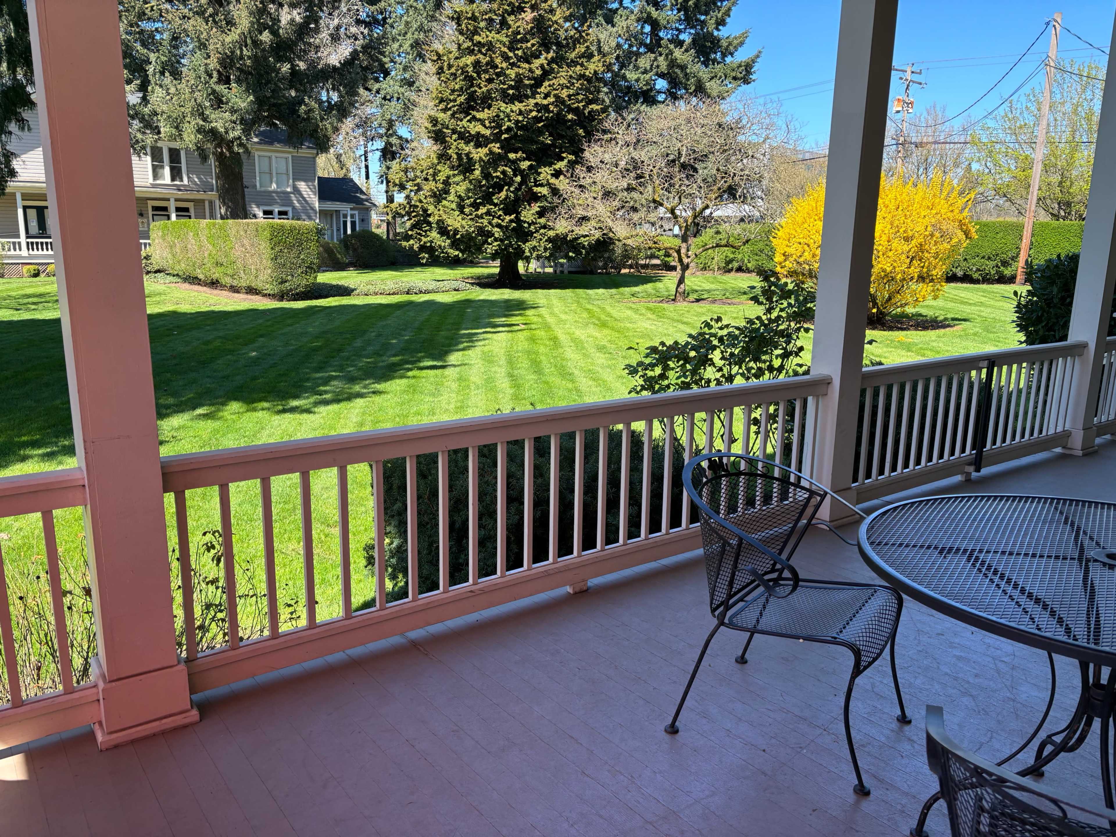 A porch with a table and chairs overlooks a well-maintained lawn and garden under a clear blue sky.