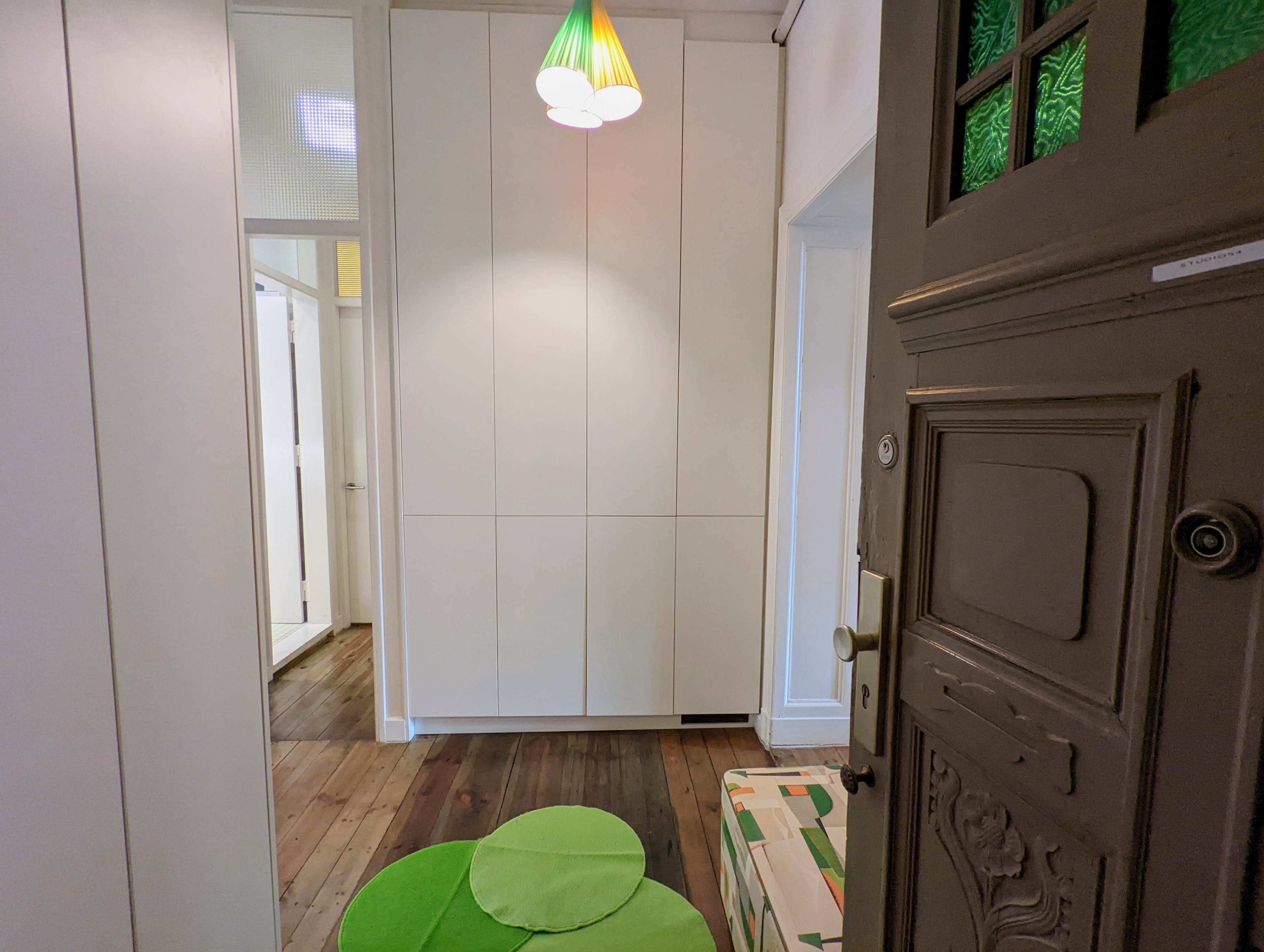 A hallway with a green pendant light, a closed door, and a green circular rug on a wooden floor.
