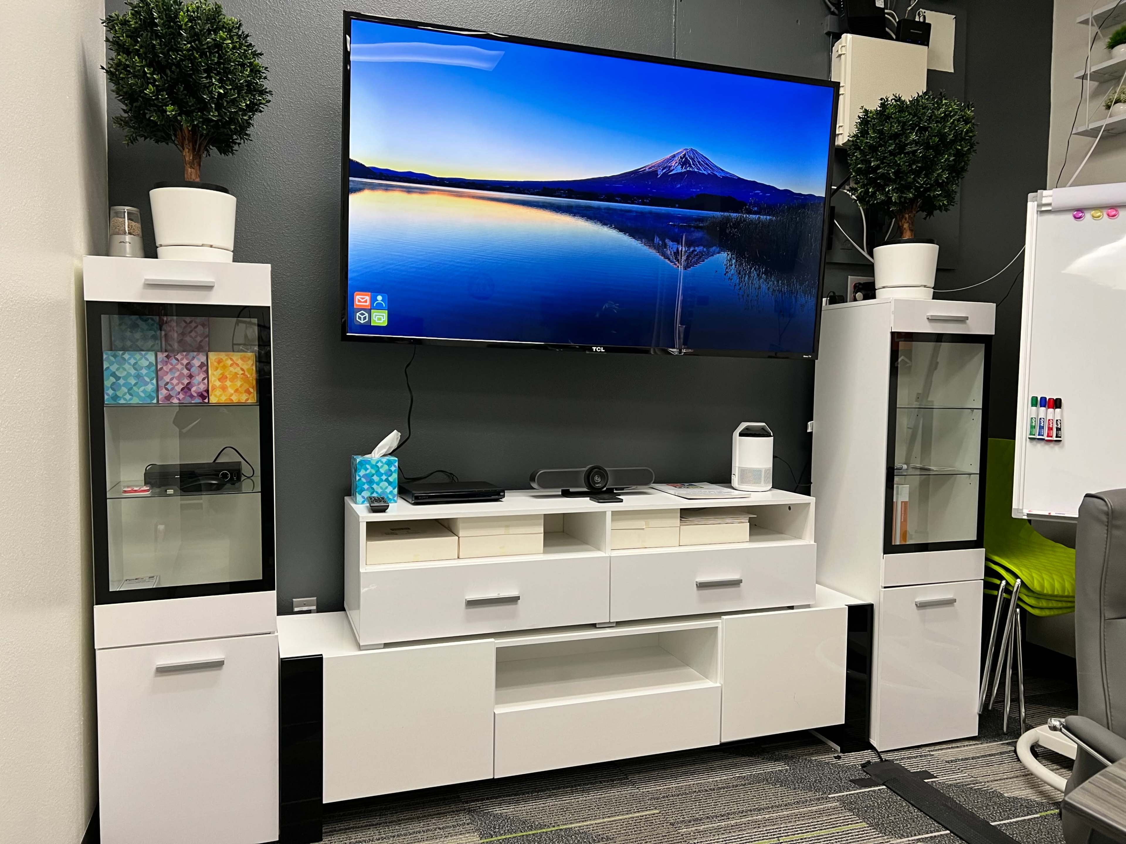 A modern living space with a large television mounted on the wall, flanked by two glass-fronted cabinets and a central media console, all set against a dark gray backdrop.