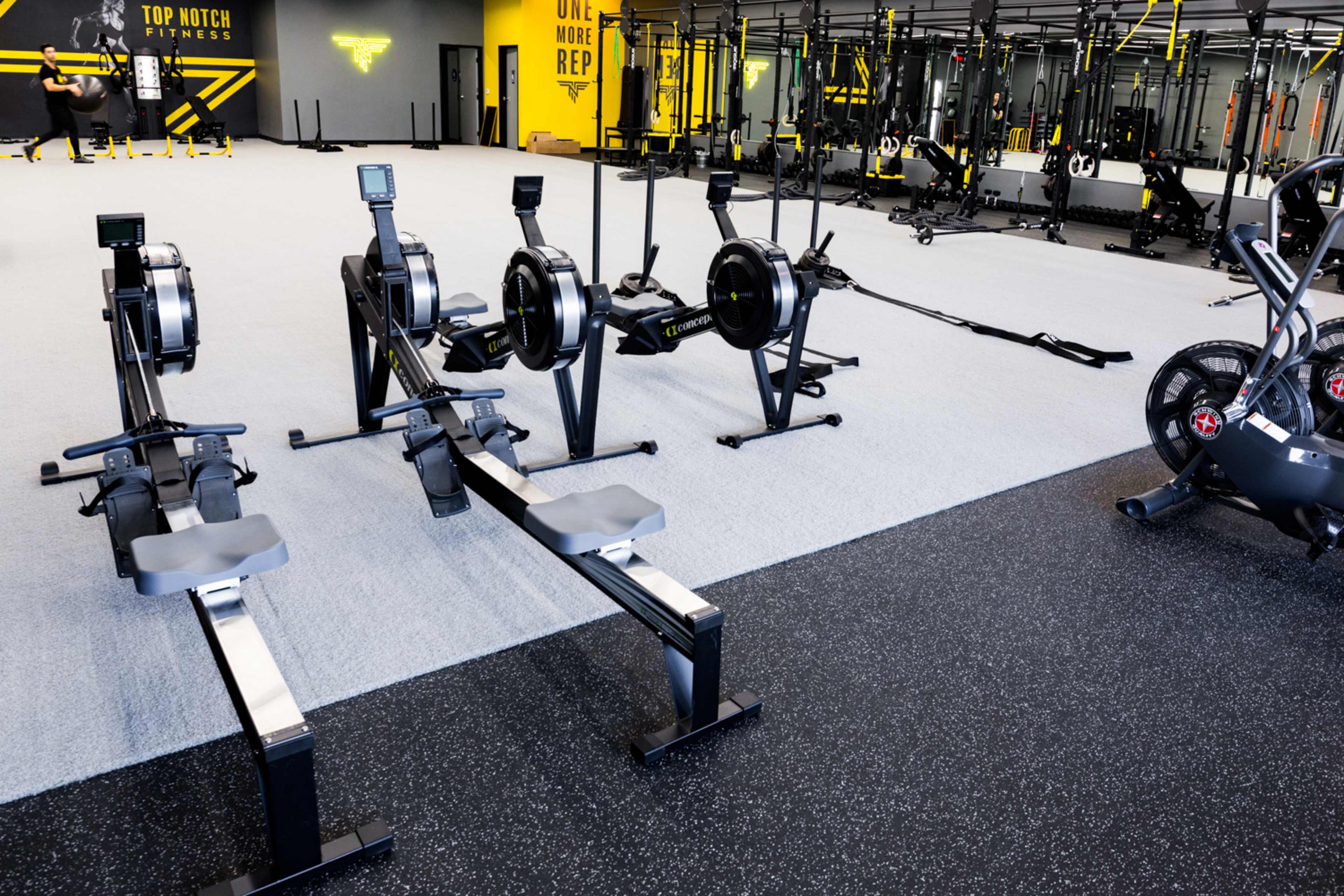 A modern gym interior featuring several rowing machines and a fitness bike on a rubberized floor.