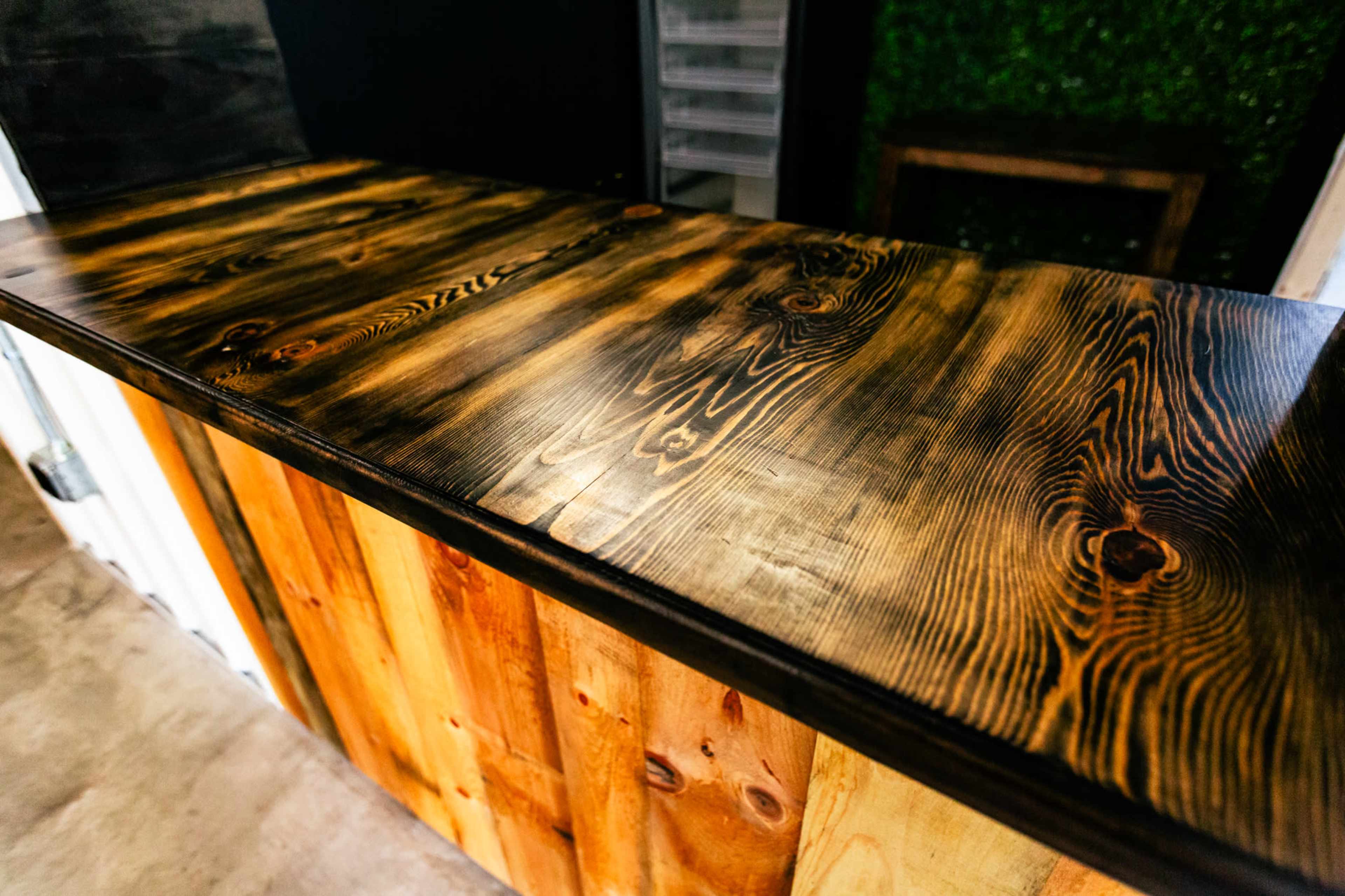 The image shows a polished wooden bar top with a contrasting texture and color between the dark and light wood grains.