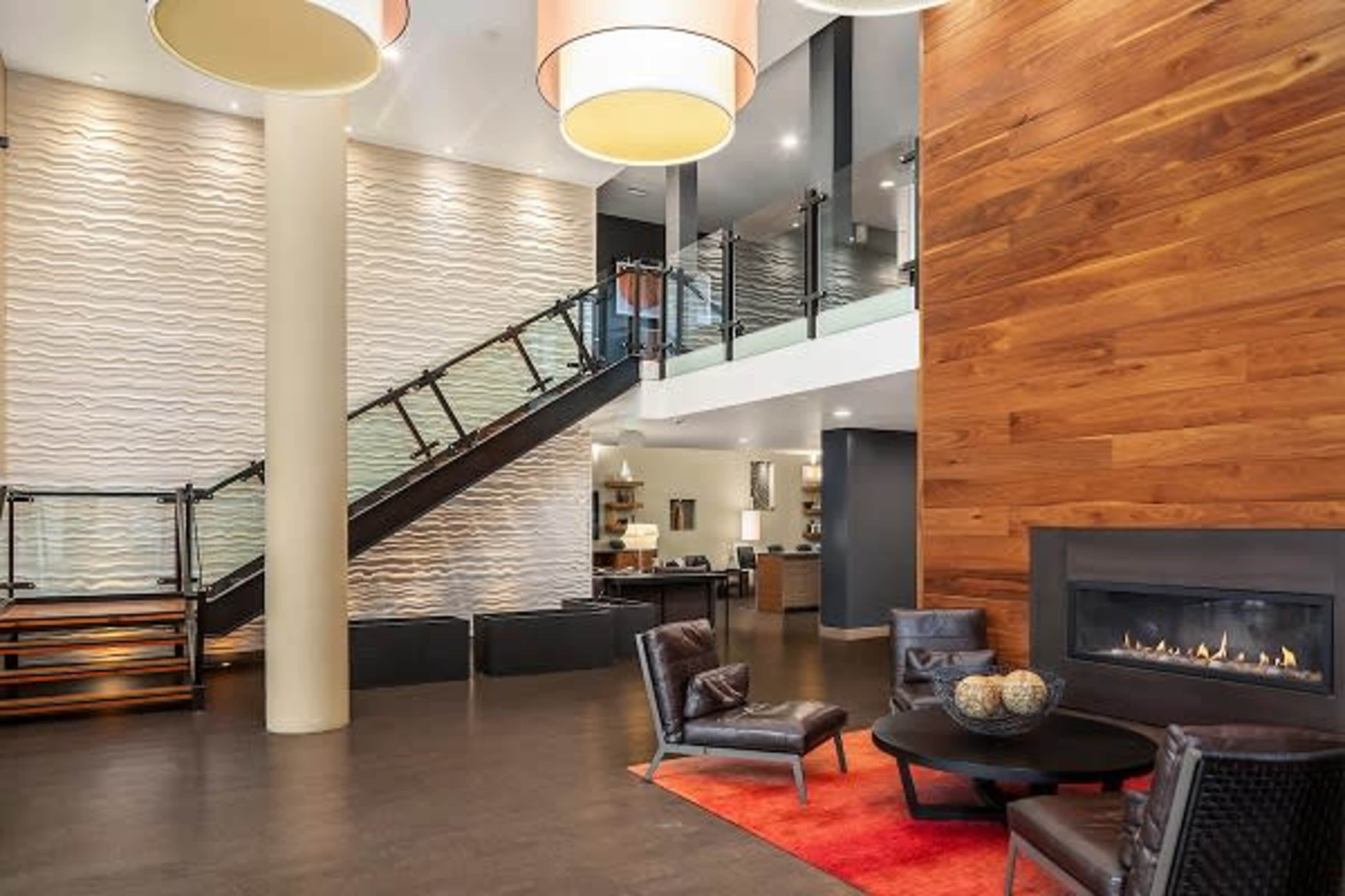 A modern lobby with a staircase, fireplace, and seating area featuring chairs and a round table.