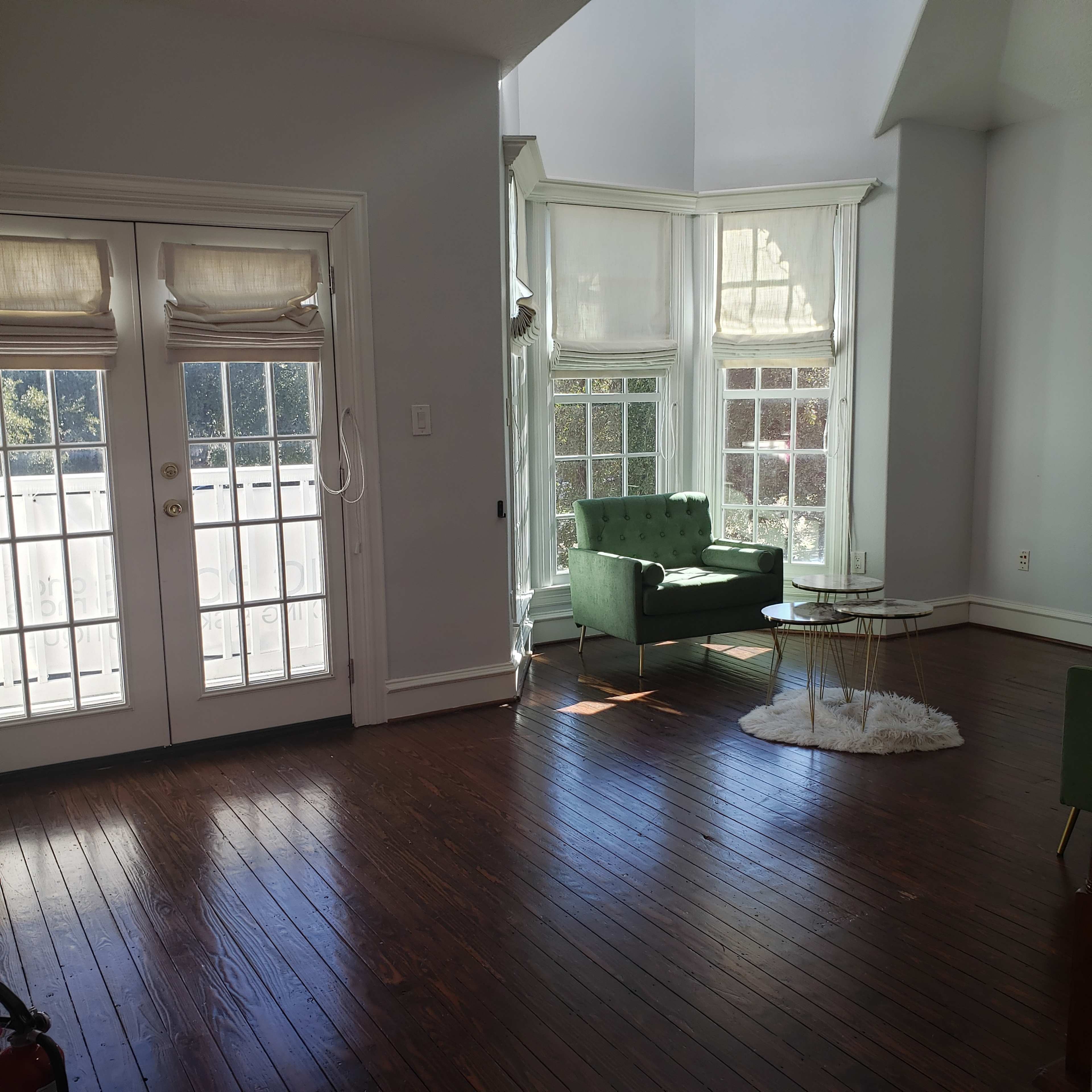 A sunlit living room features a green armchair, a small glass table, and large windows with white curtains.