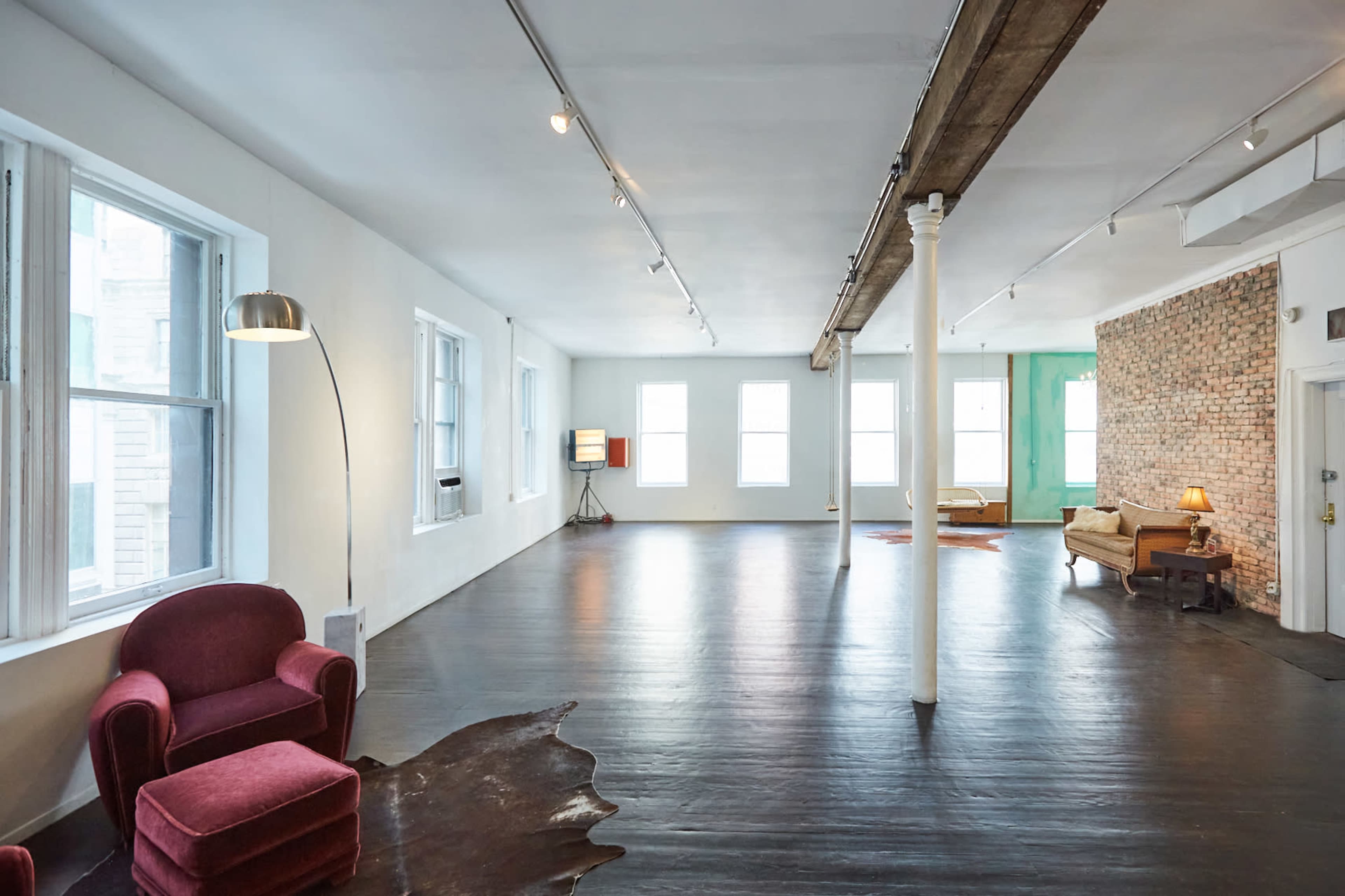 A spacious, empty room with large windows, a brick wall, and various seating arrangements.