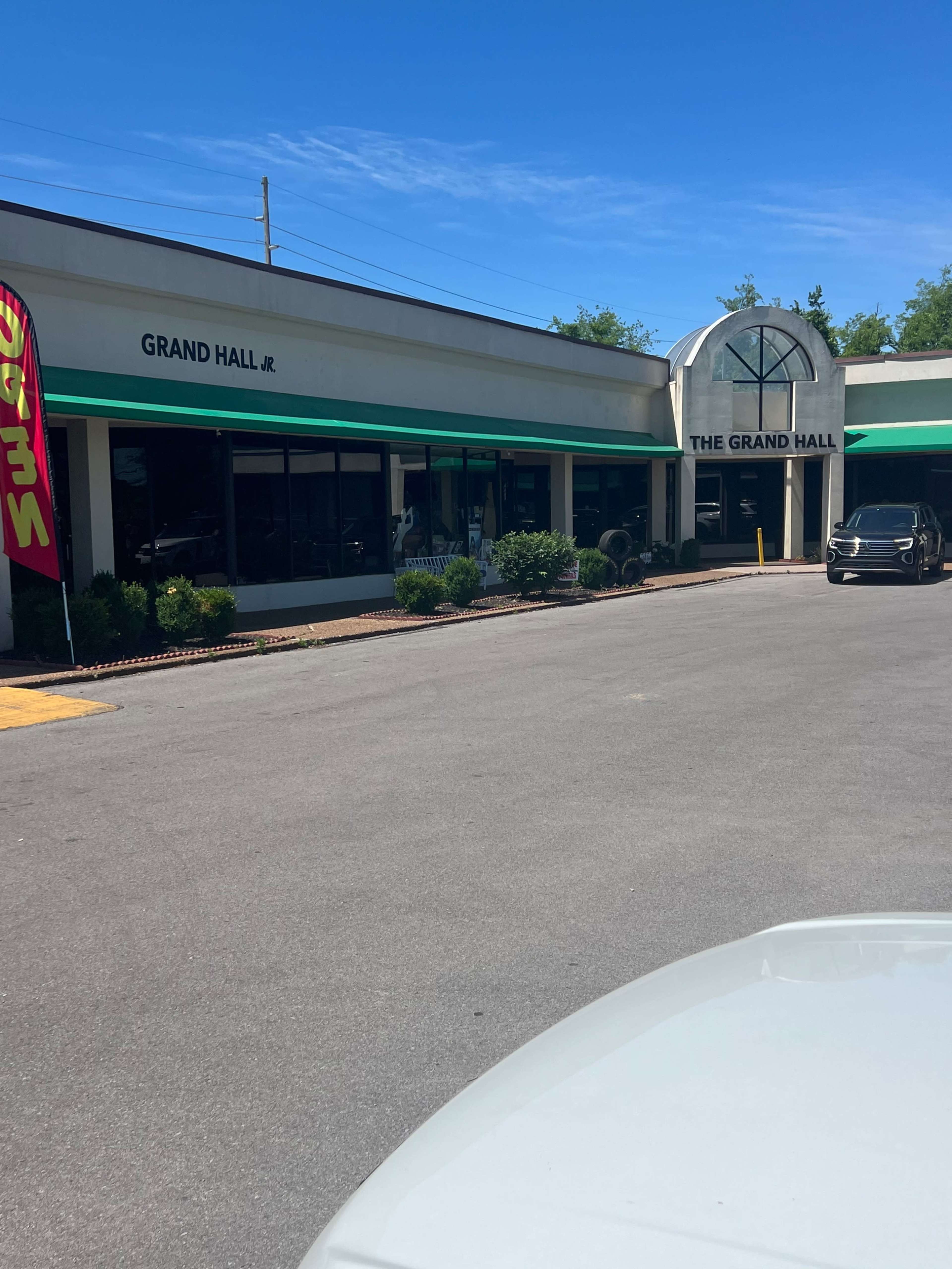 A commercial building labeled "Grand Hall" and "Grand Hall Jr." with a parking area in front and clear blue skies above.