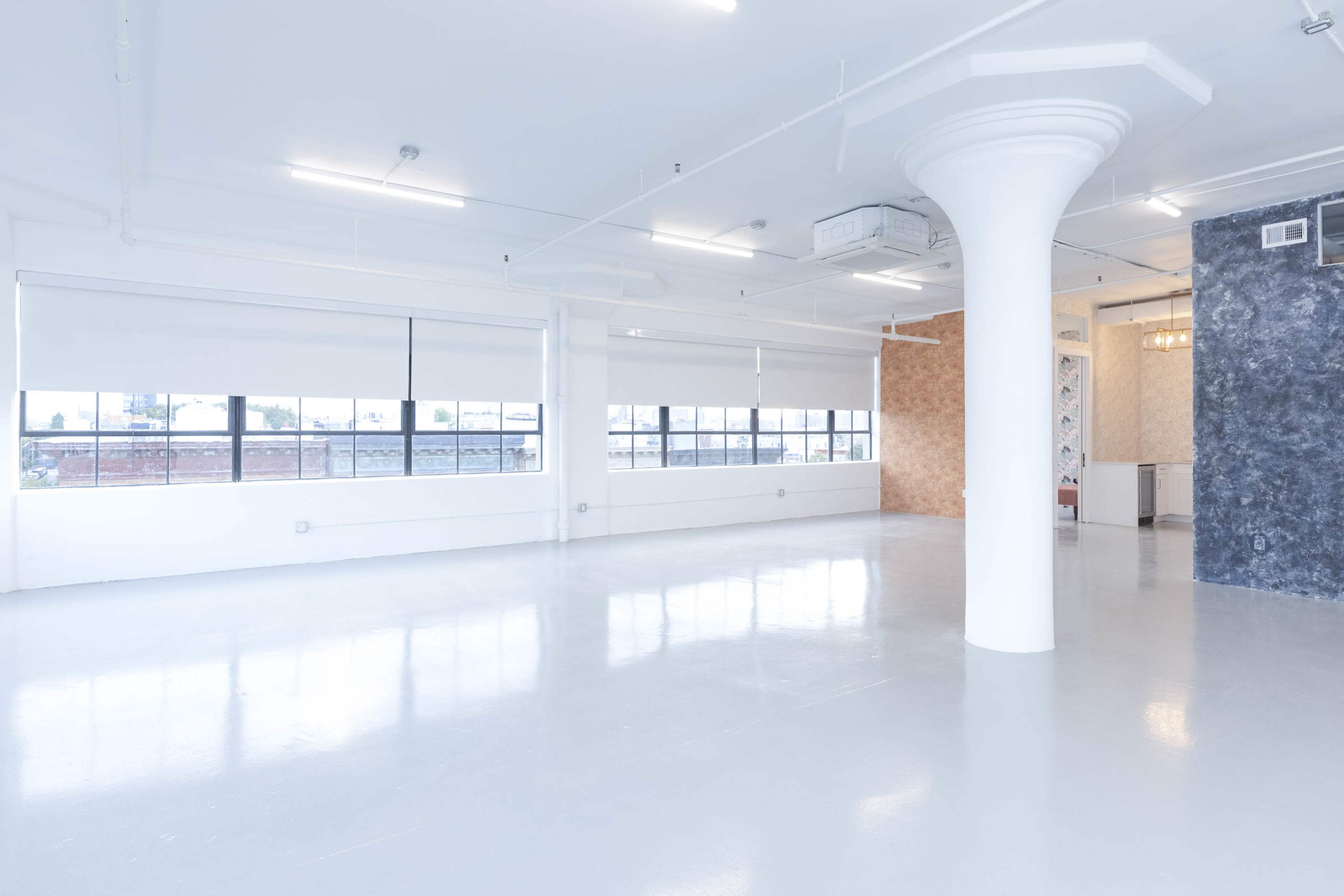 An empty, well-lit room with polished concrete floors, large windows, and a central white column.