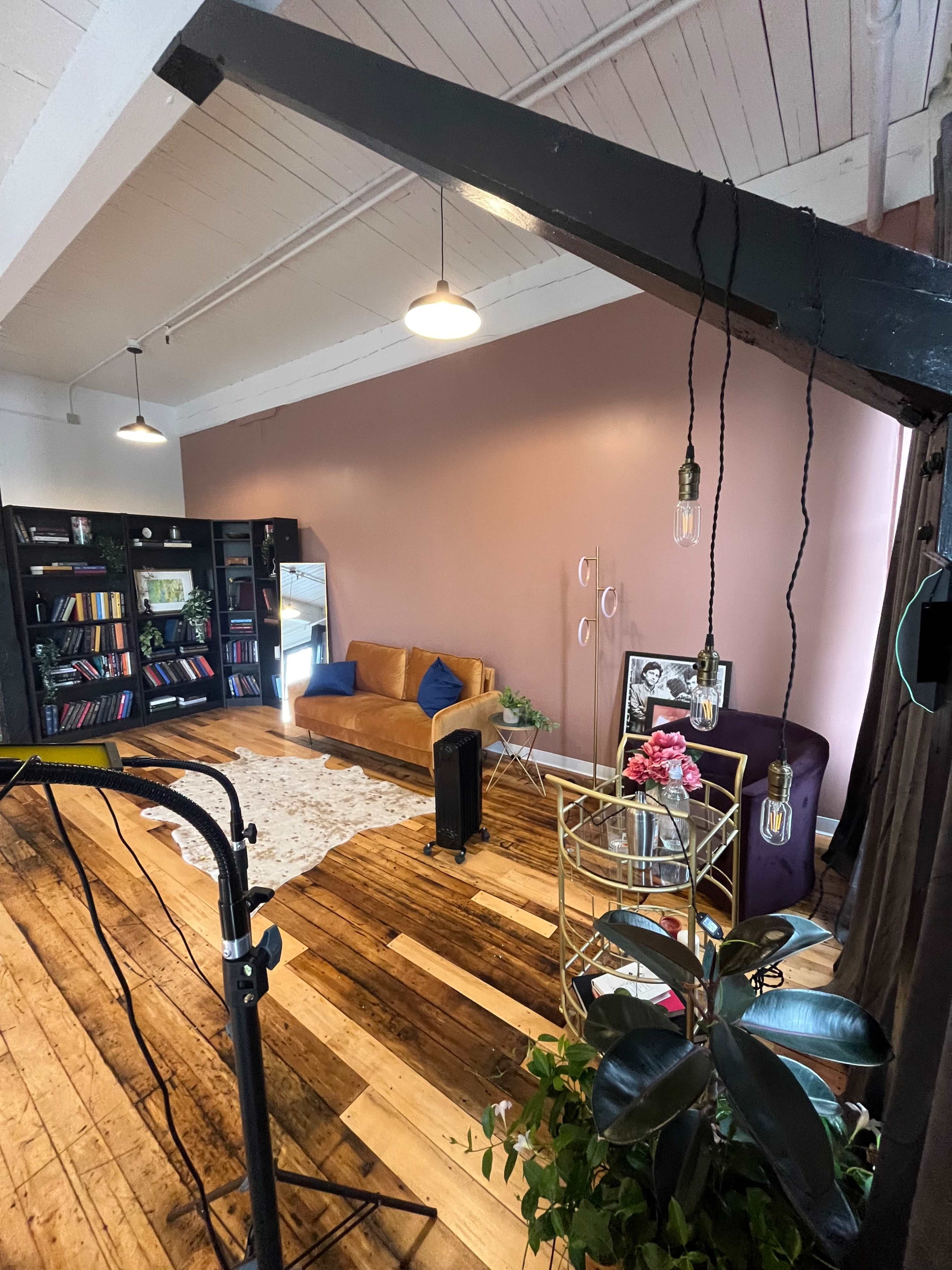 A spacious room with wooden floors, a brown sofa, a bookshelf filled with books, and decorative plants.