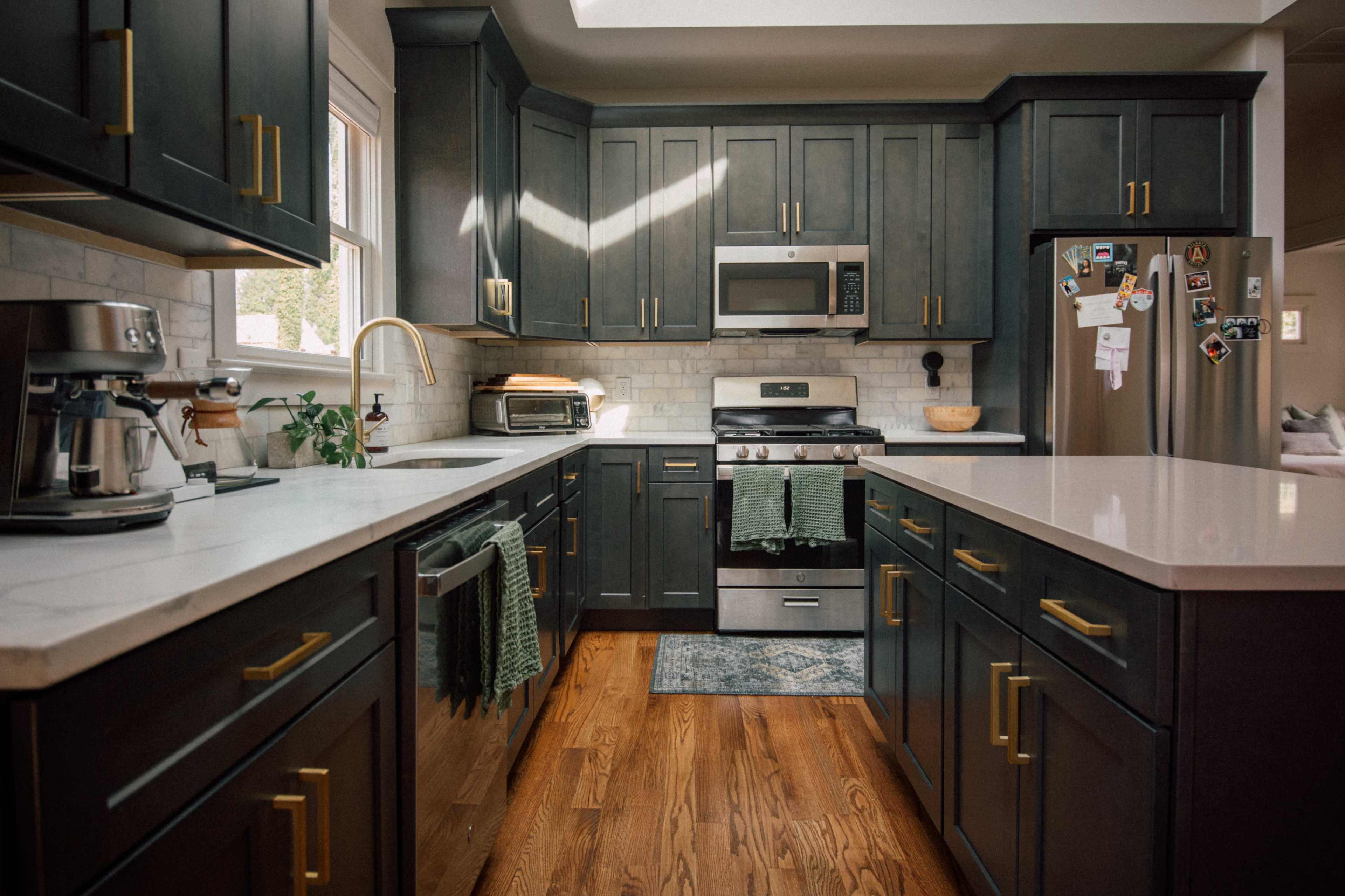 A modern kitchen features dark cabinetry, stainless steel appliances, and a central island with a white countertop.