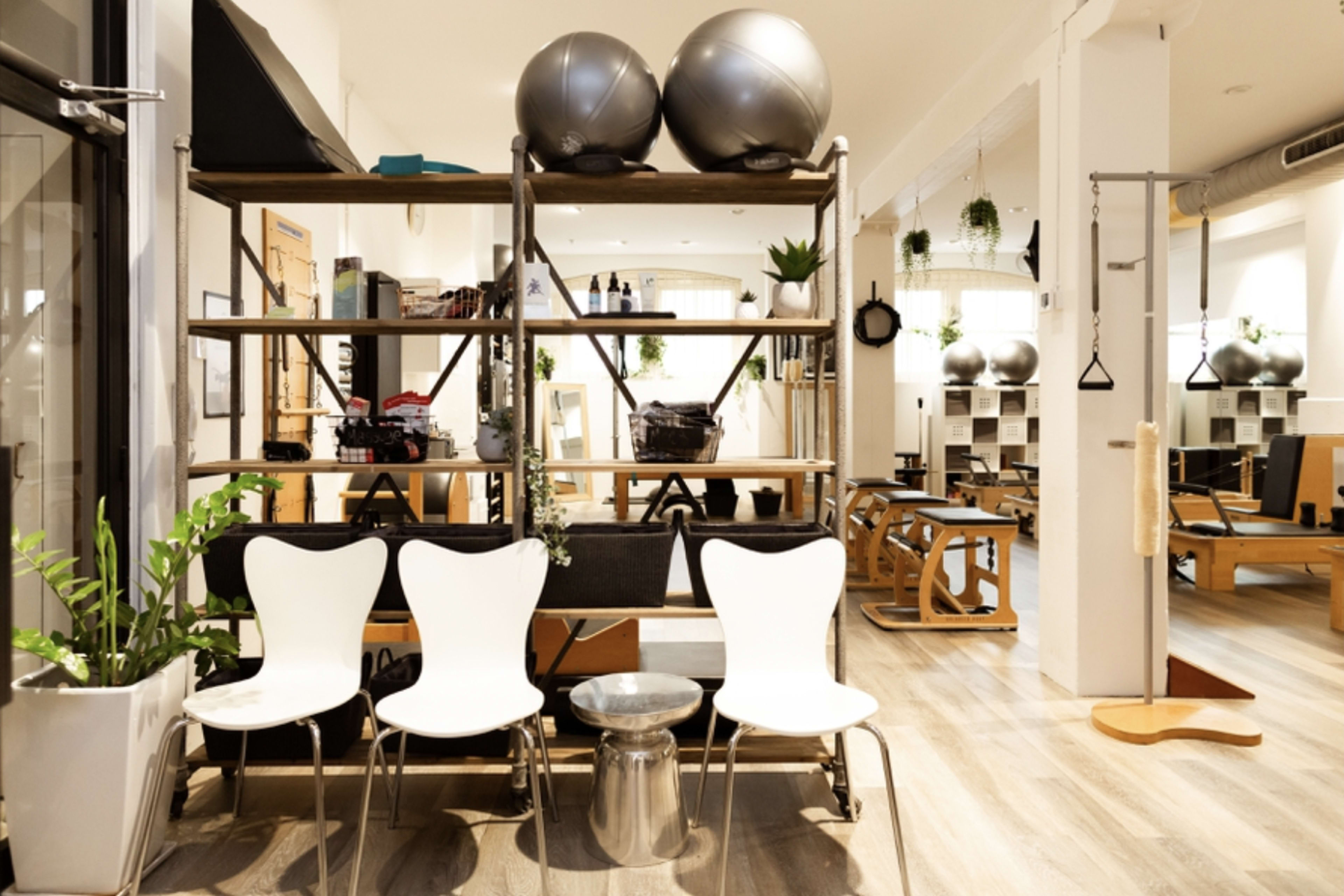 A modern fitness studio with wooden shelving, exercise equipment, and a row of white chairs in front.