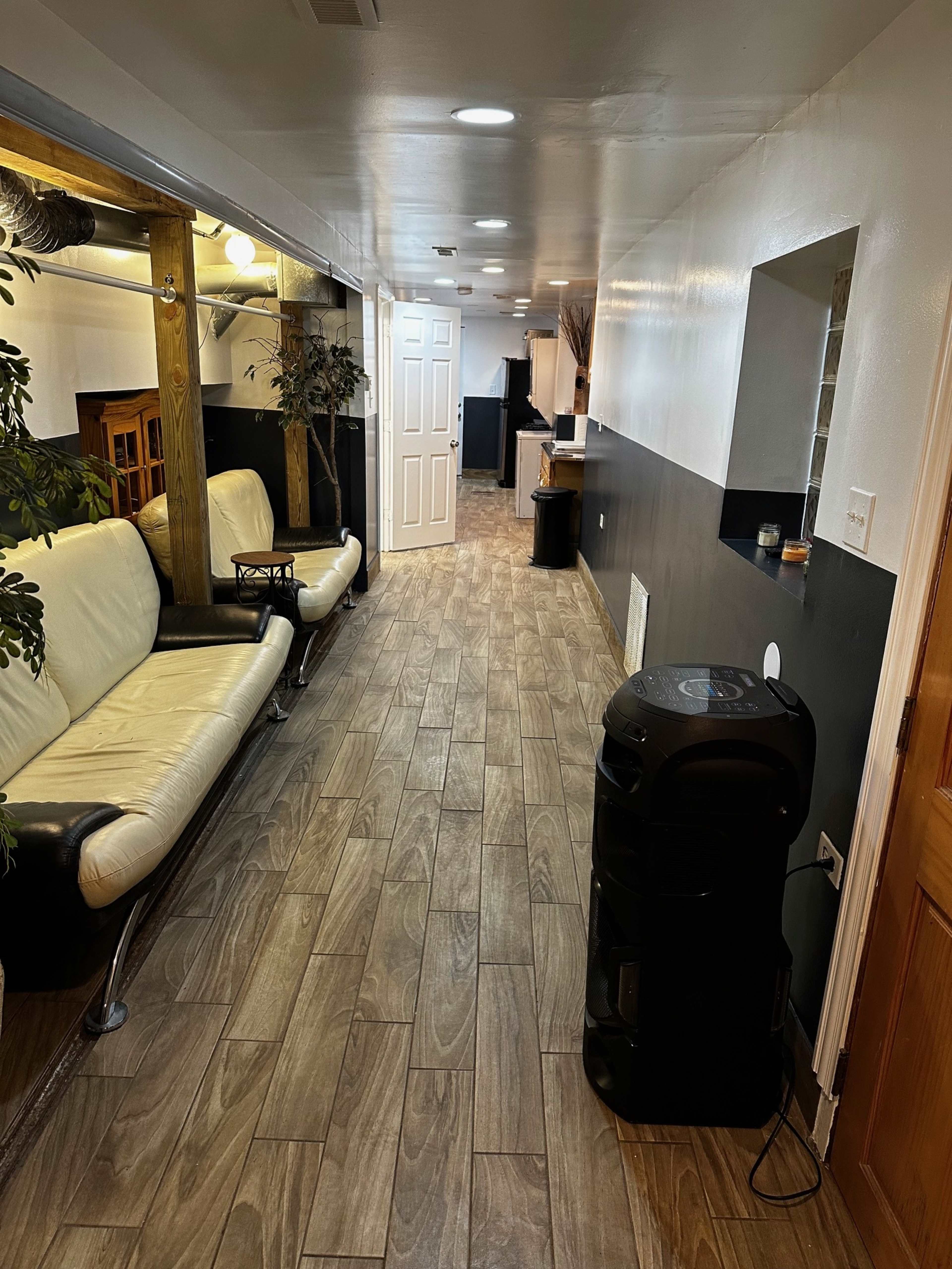 The image shows a long, narrow hallway with a white and black color scheme, featuring a sofa on one side and a doorway at the end.