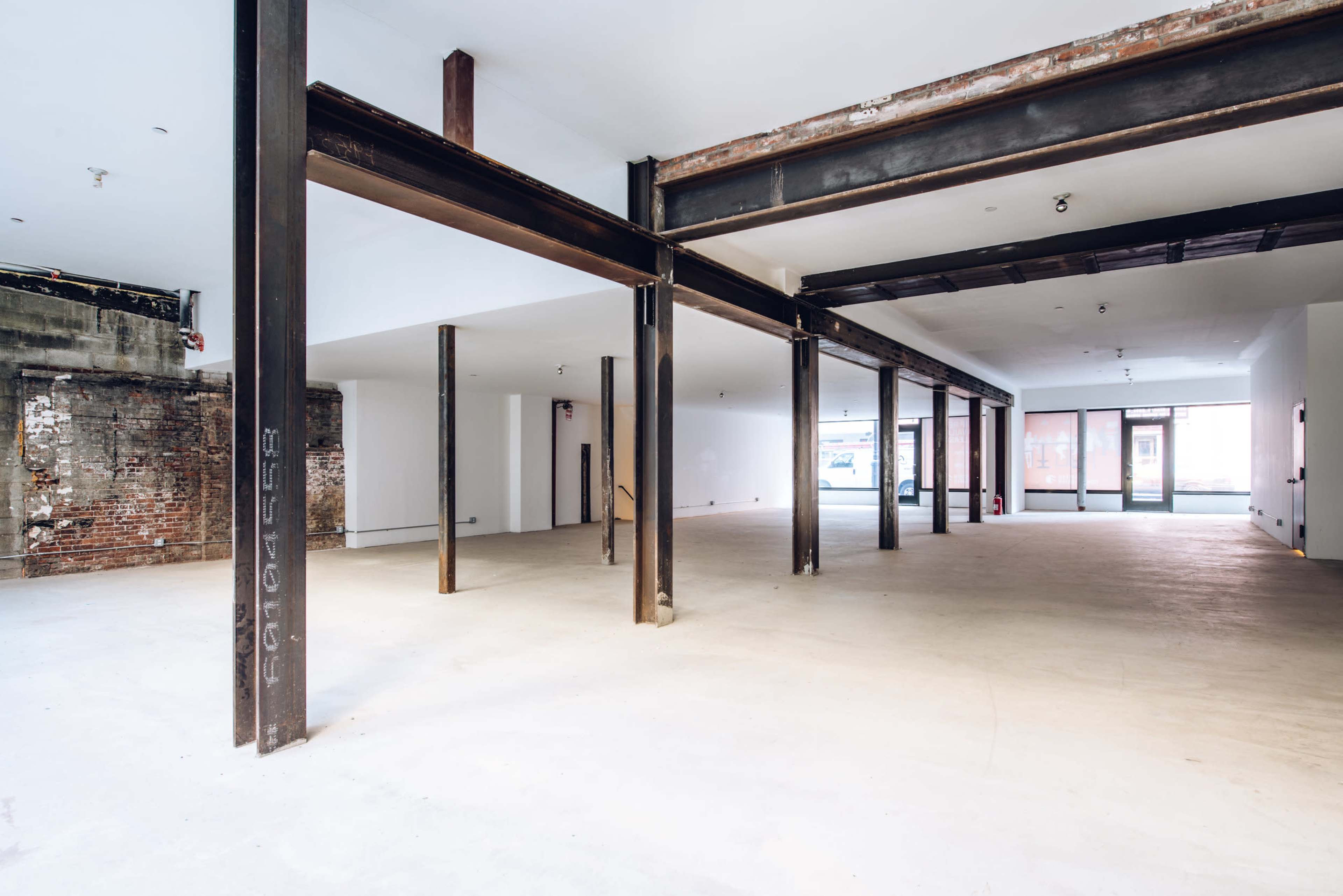 The image shows an empty industrial space with exposed steel beams and a concrete floor.