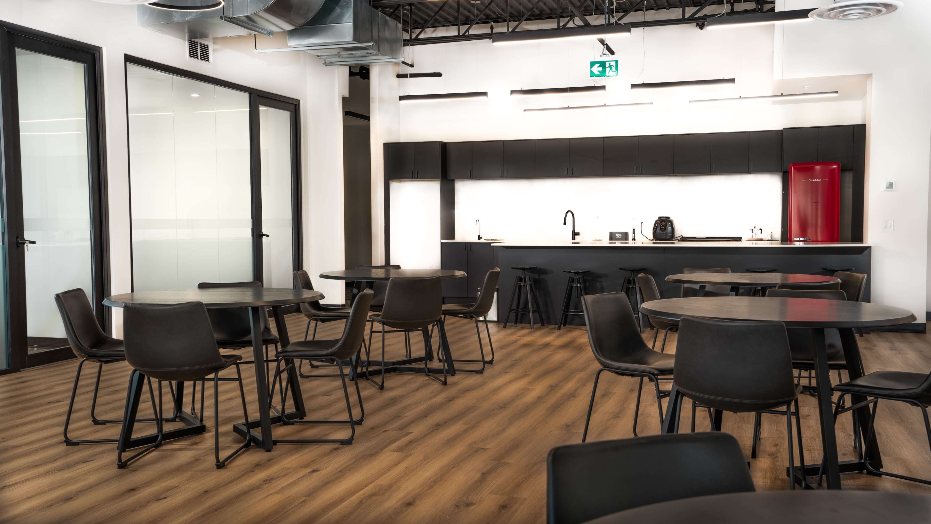 A modern kitchen and dining area with black tables and chairs, wooden flooring, and a sleek kitchen with a red refrigerator and appliances.