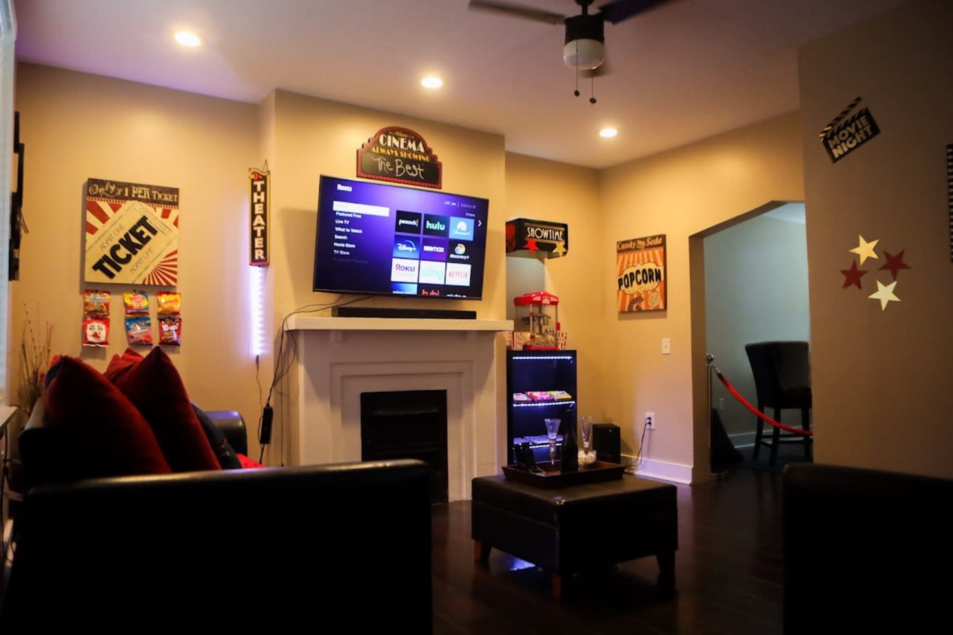 A cozy home theater setup with a white fireplace, a large TV displaying streaming options, and decor featuring popcorn and ticket themes on the walls.