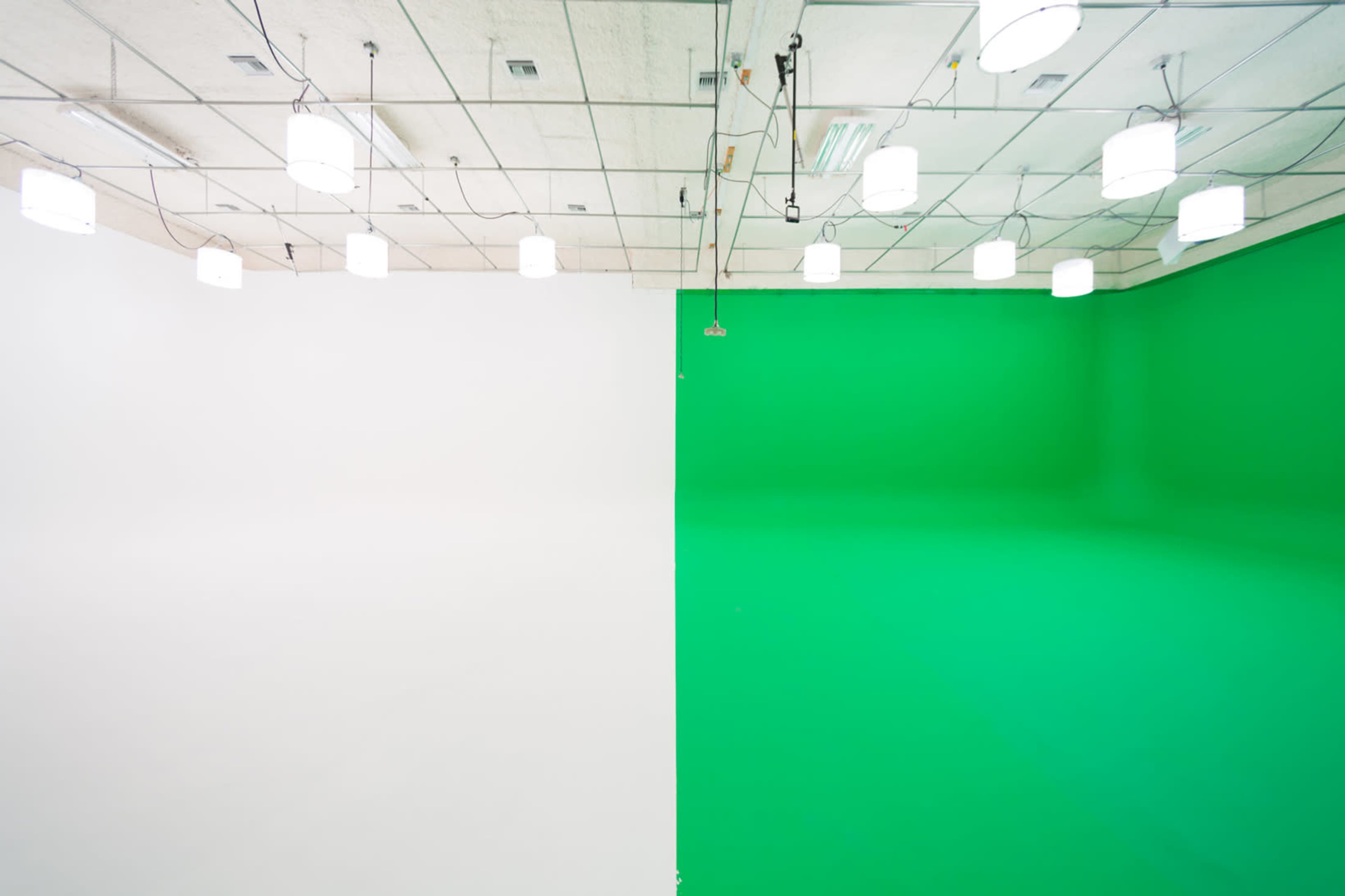 A studio space divided into two sections, one with a white wall and the other with a green wall, illuminated by overhead lights.