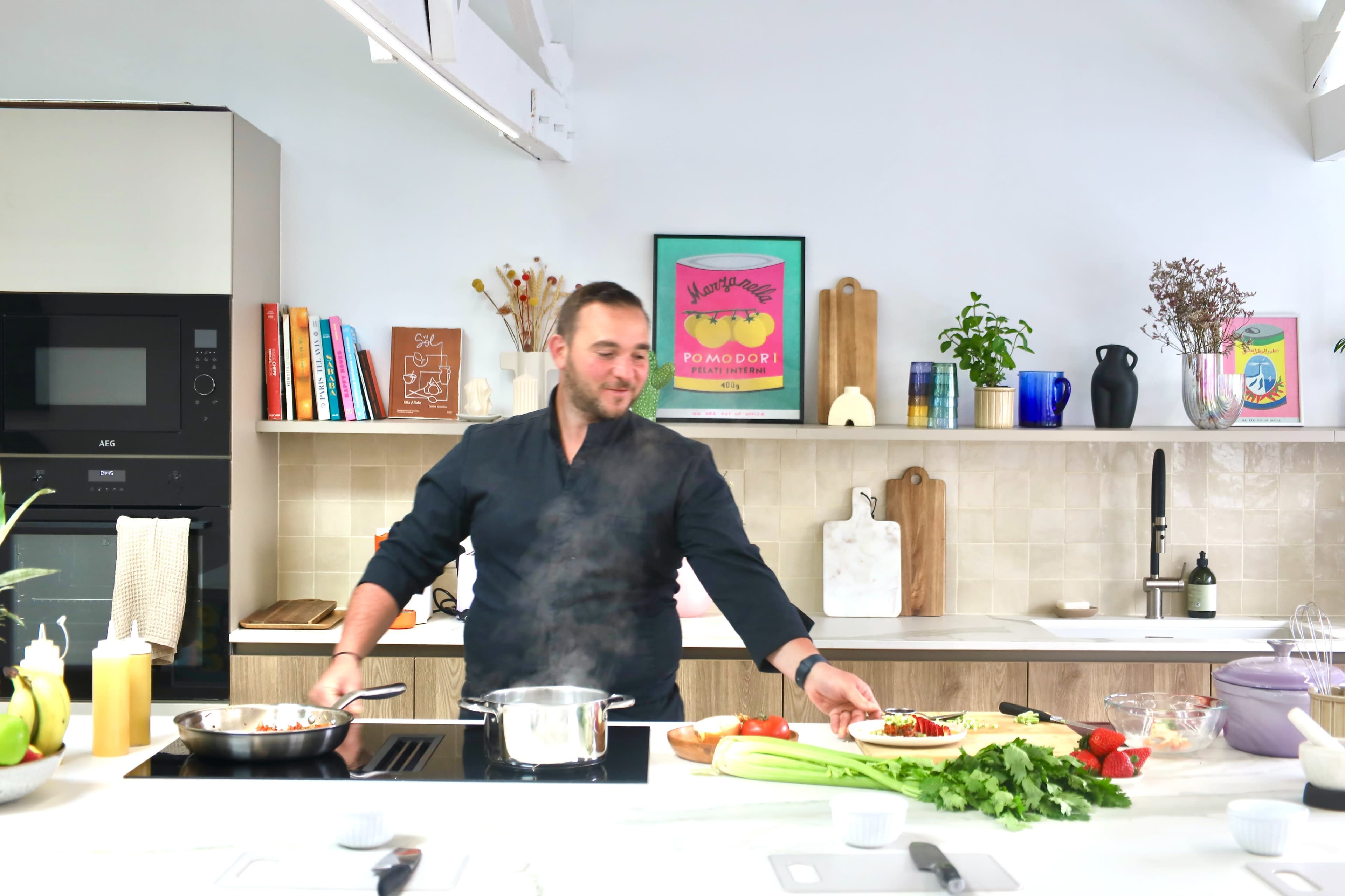 A man in a black shirt prepares food on a countertop in a bright kitchen with various ingredients and cooking utensils.