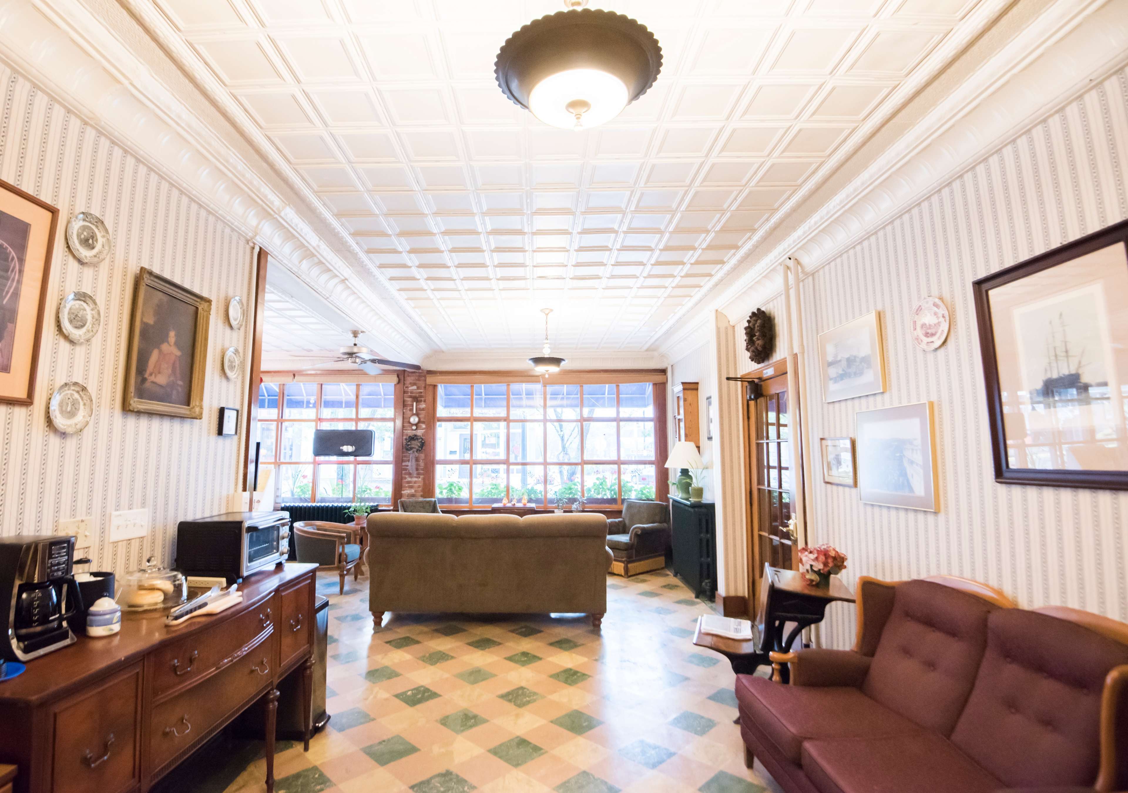 A spacious living room with patterned tile flooring, a ceiling with decorative tiles, and large windows allowing natural light to enter.