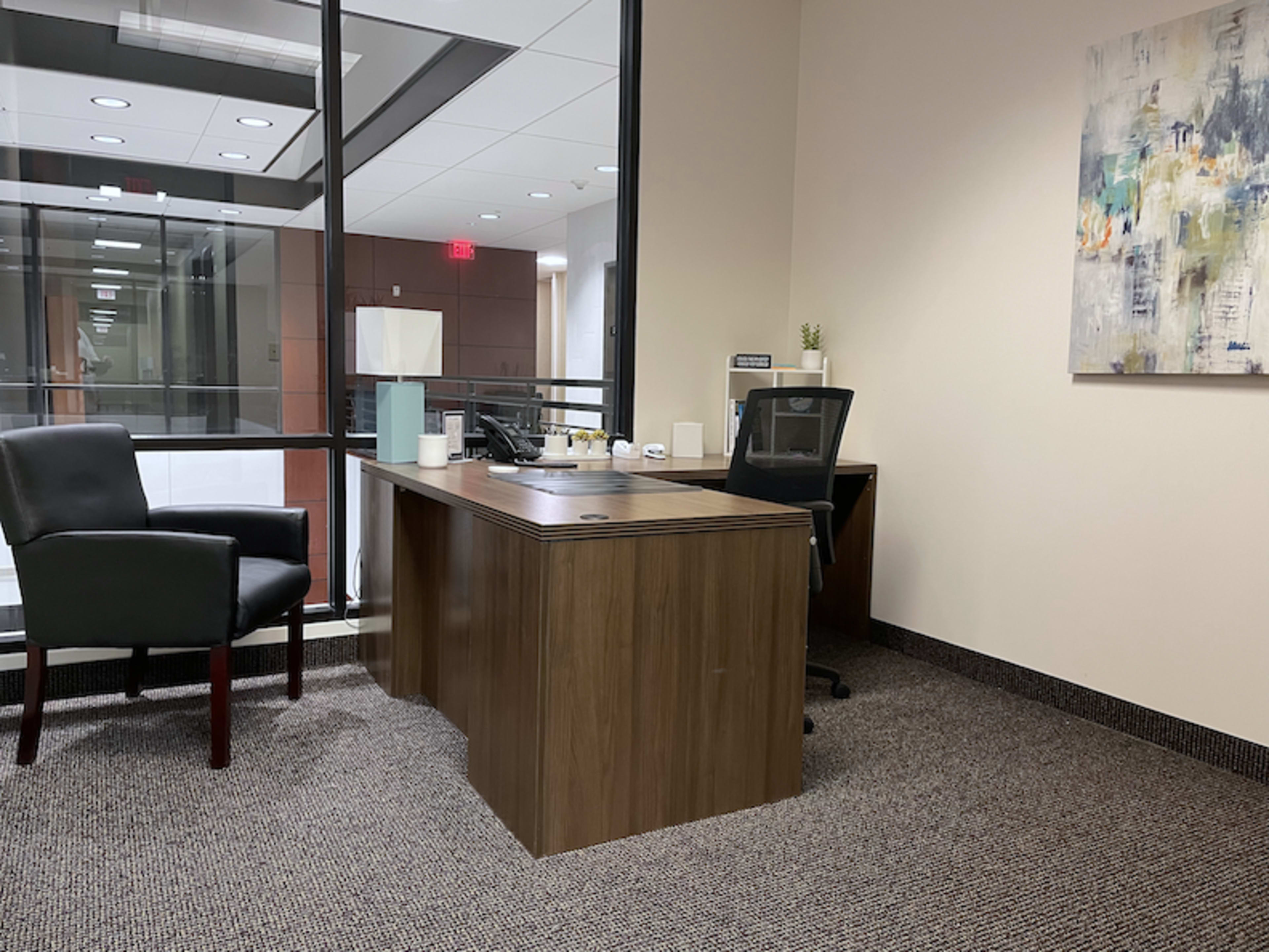 The image shows a modern office space featuring a wooden desk, a black chair, a phone, and a decorative painting on the wall.