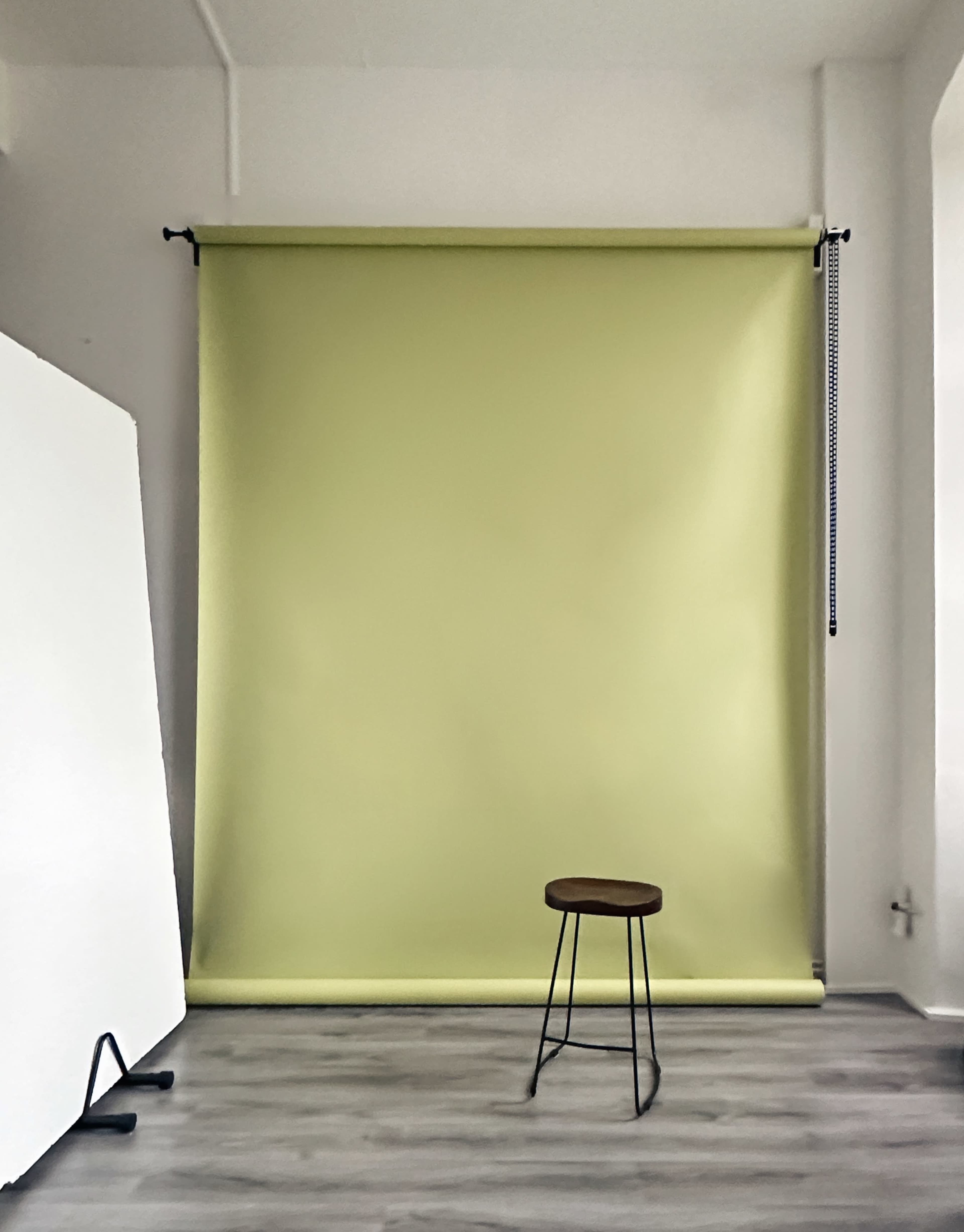 The image features a studio space with a light green backdrop and a wooden stool in front of it, alongside a white reflector on the left.