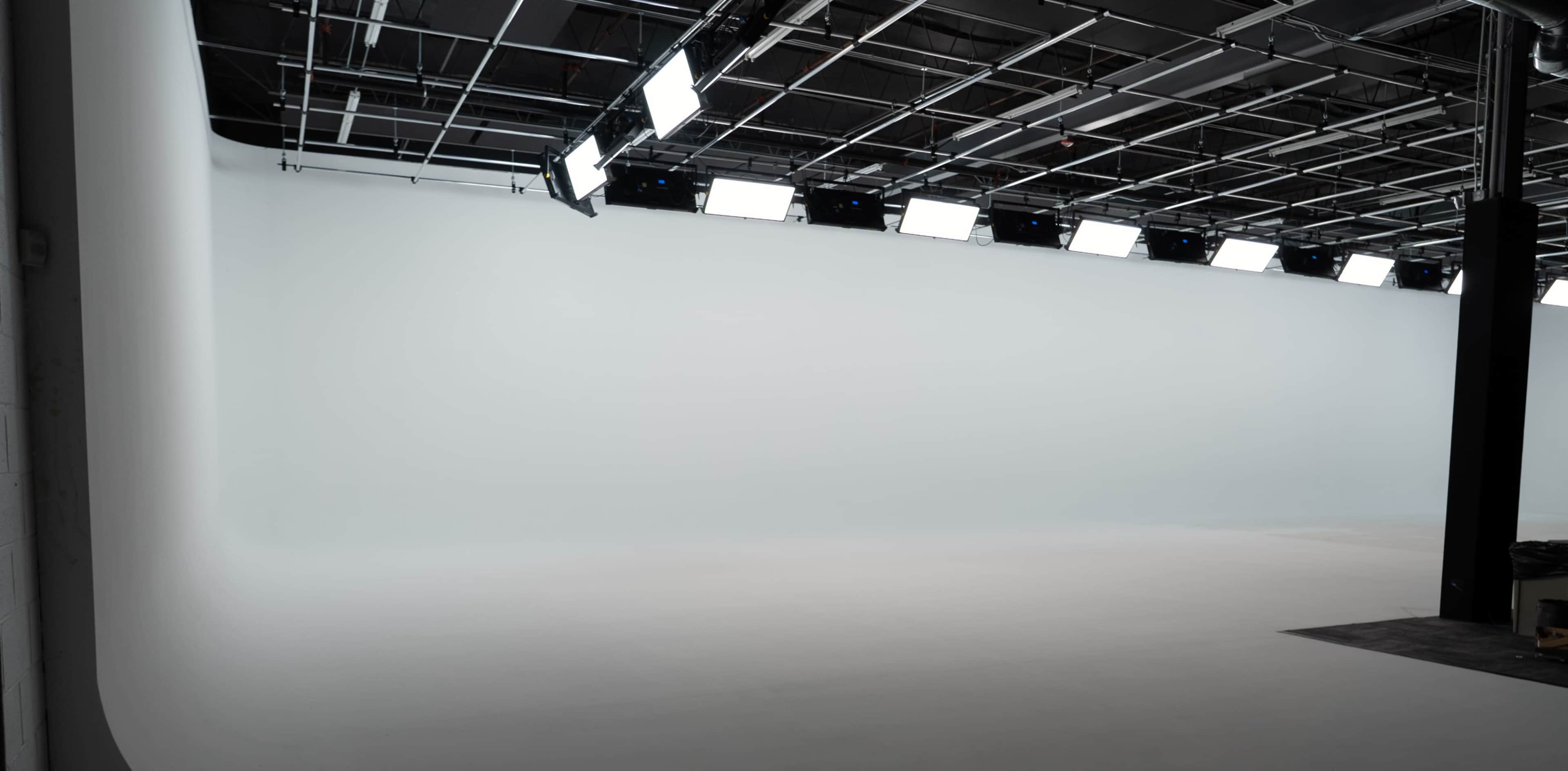 A well-lit photography studio features a large, blank white backdrop and a grid of overhead lights.