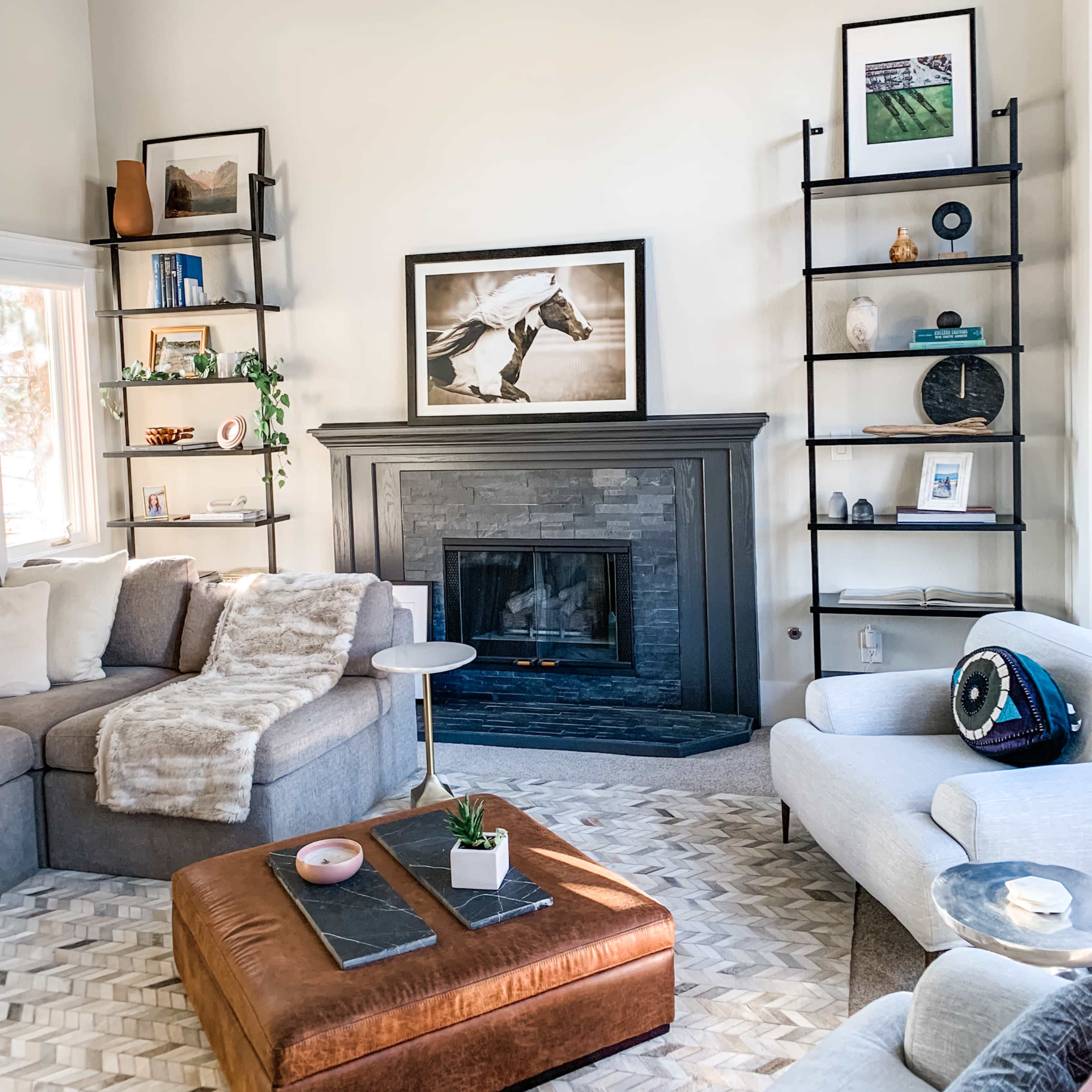 The image shows a living room with a fireplace, surrounded by bookshelves, a large sectional sofa, and an ottoman in earthy tones.