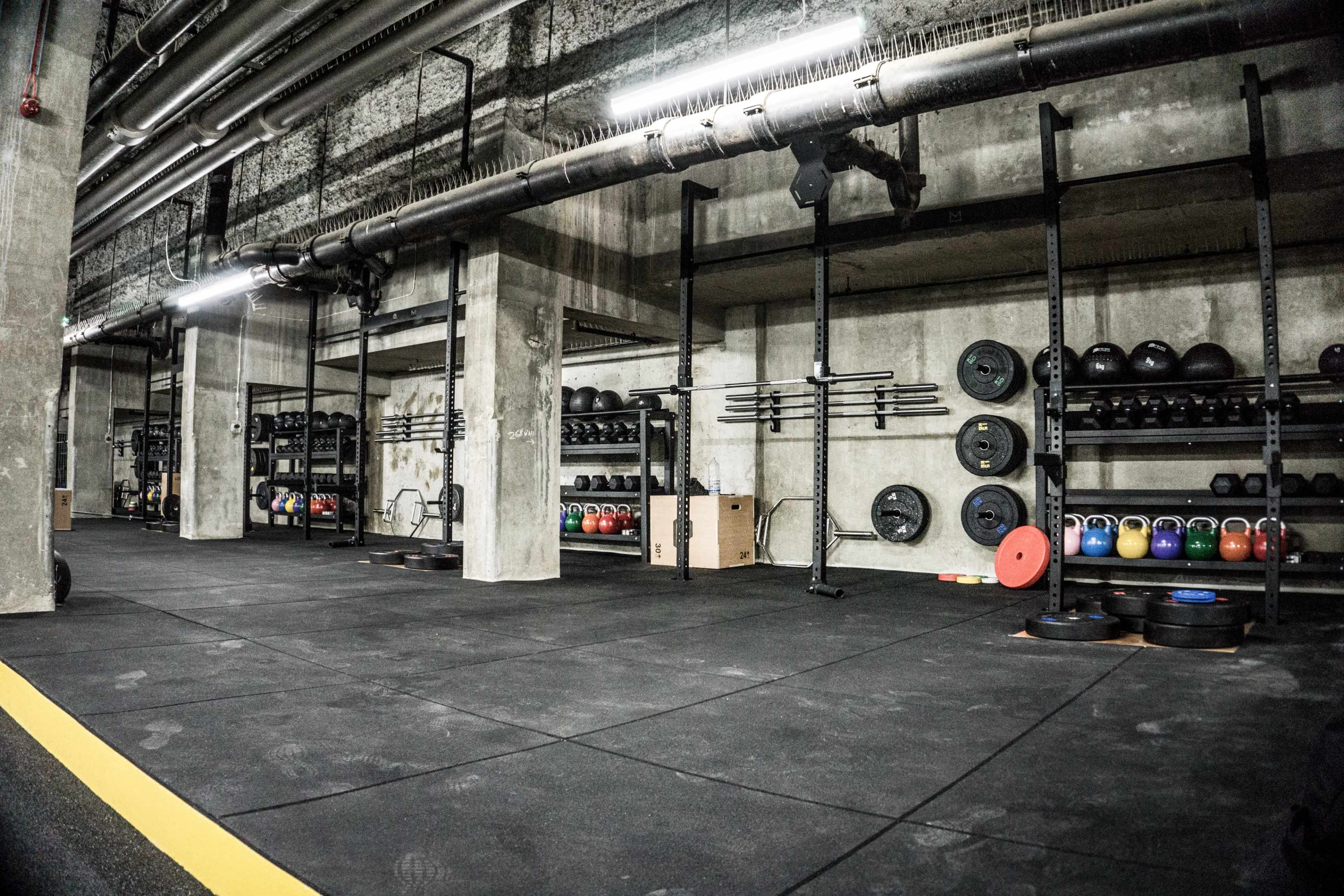 The image shows a spacious gym with various weightlifting equipment and rubber flooring.