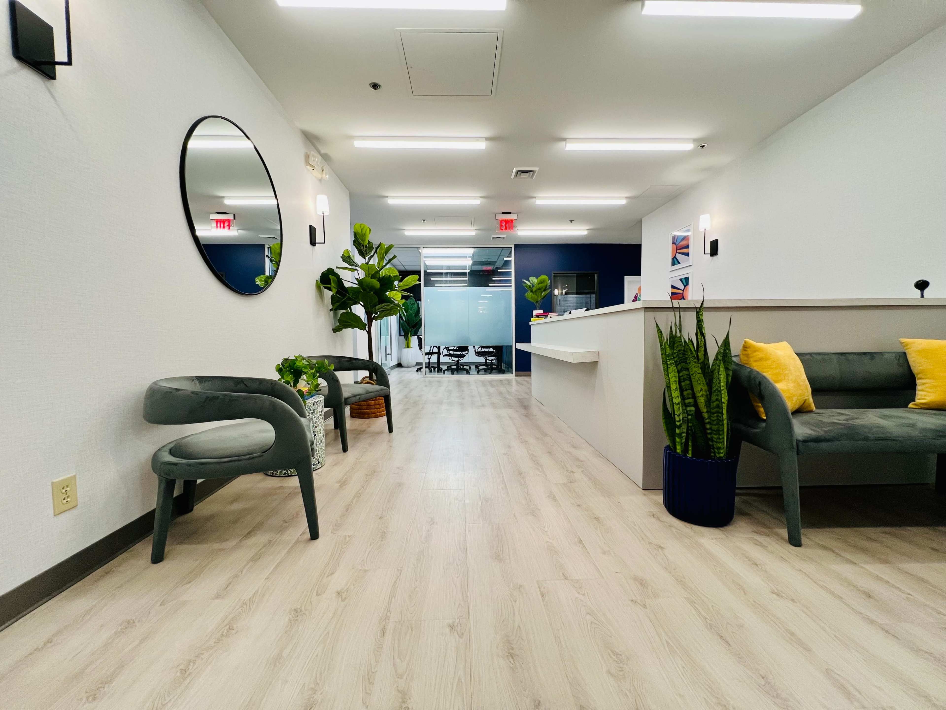 A modern reception area with chairs, plants, and a front desk in a well-lit hallway.