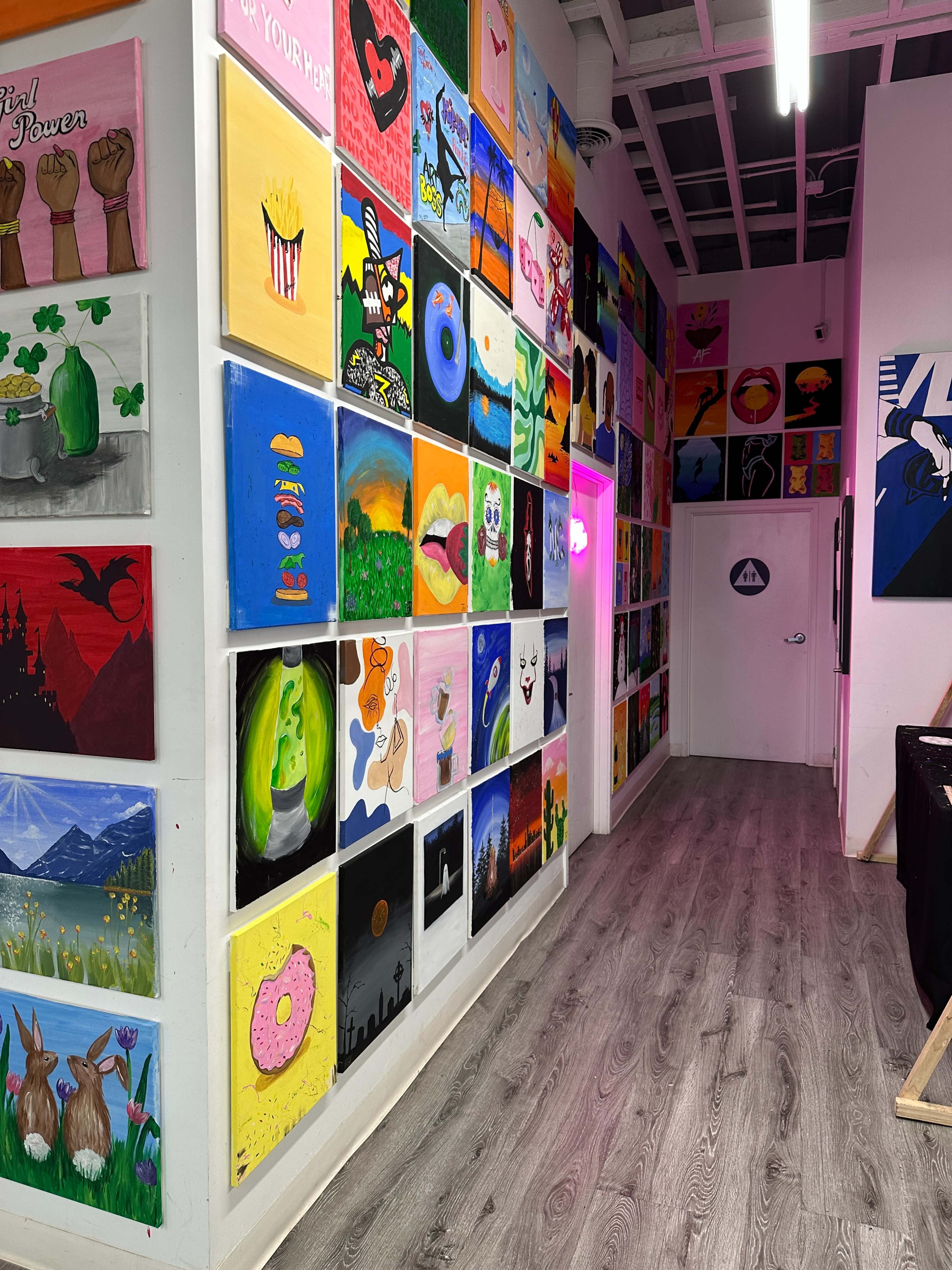 The image shows a hallway adorned with colorful paintings displayed on the walls, leading to a door at the end.