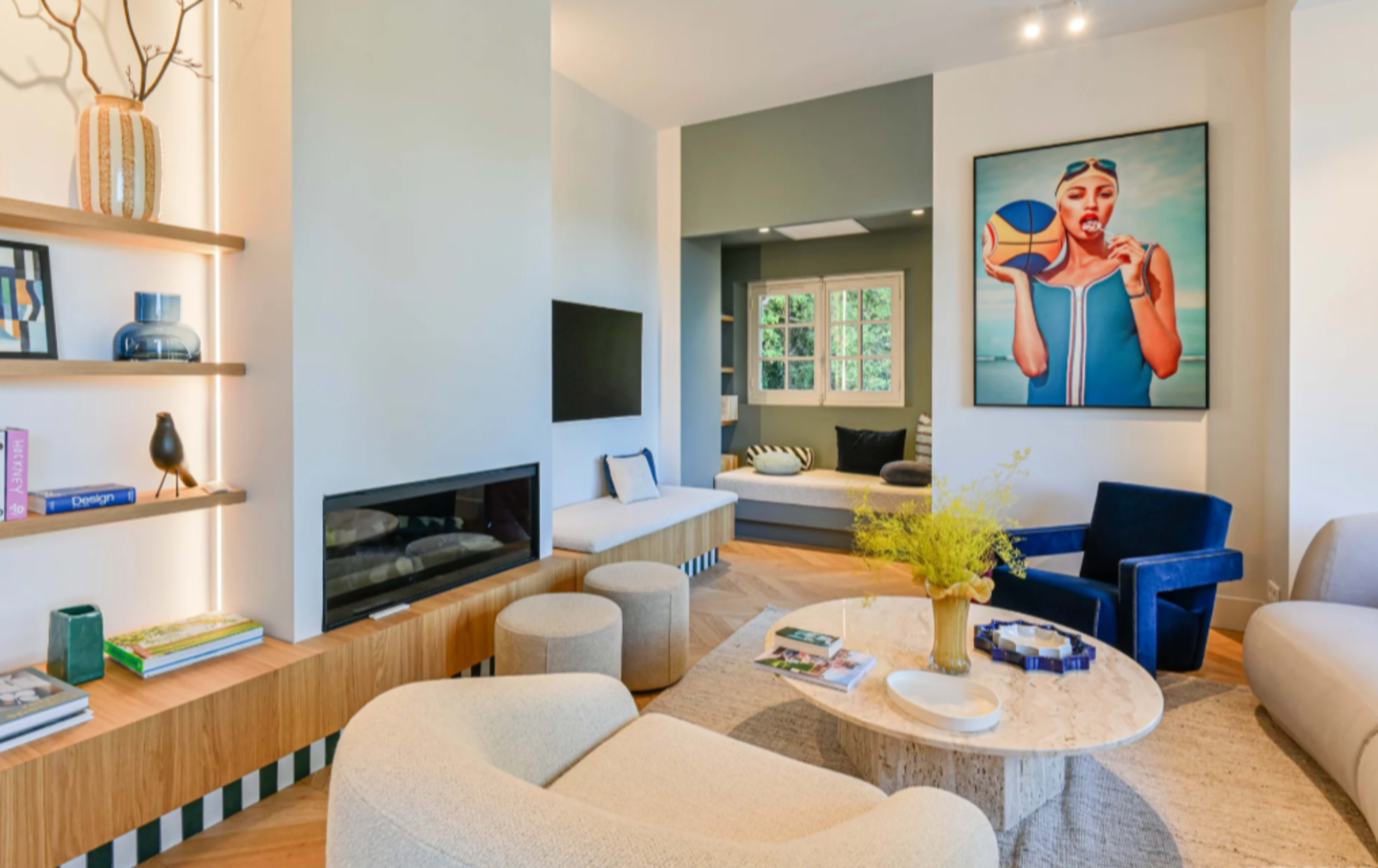 The image showcases a modern living room featuring a large artwork, a light-colored seating arrangement, and a minimalist decorative setup with a fireplace and shelves.