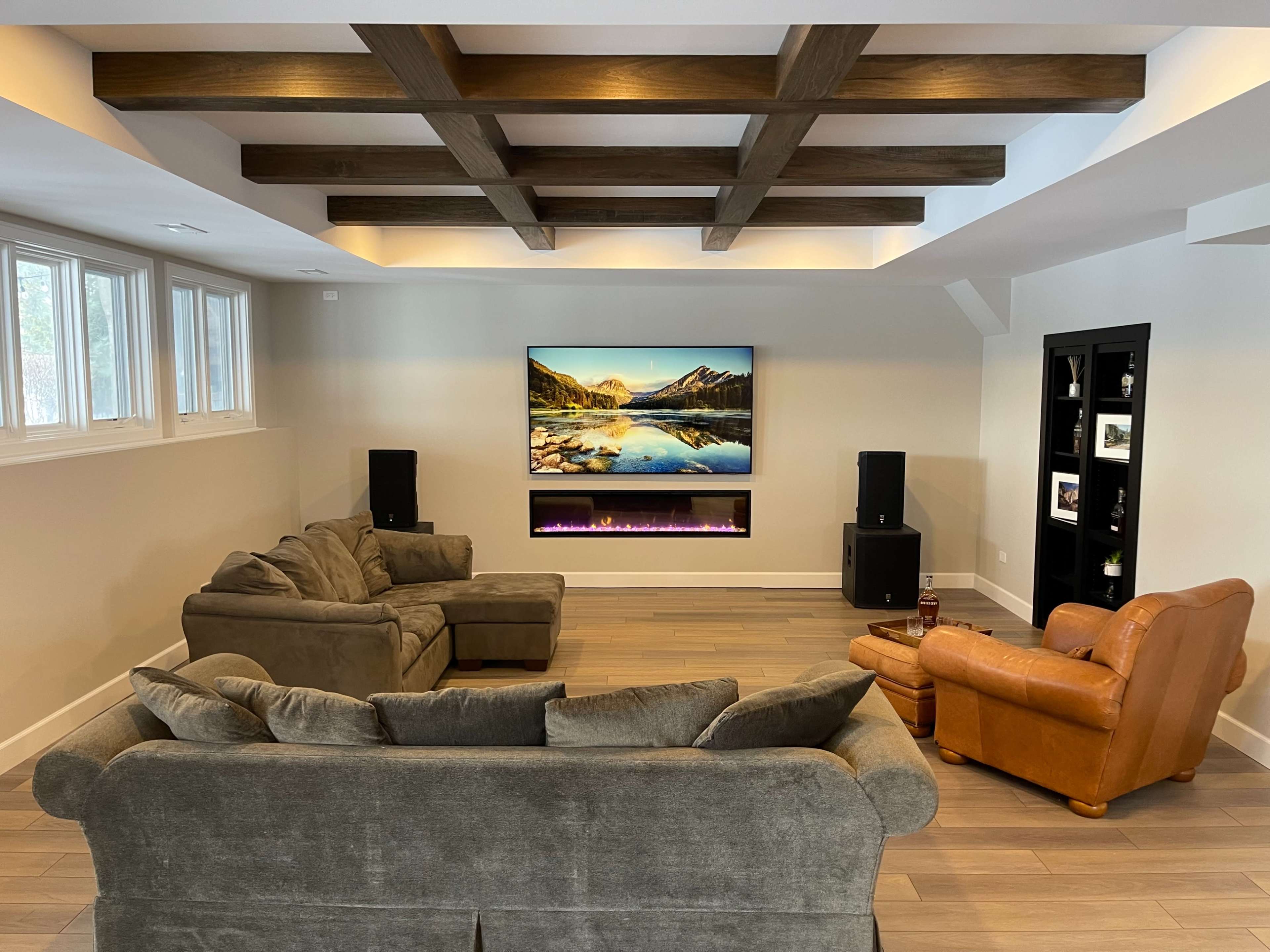 The room features a set of comfortable sofas arranged around a wall-mounted television with a scenic landscape display and an electric fireplace below it.