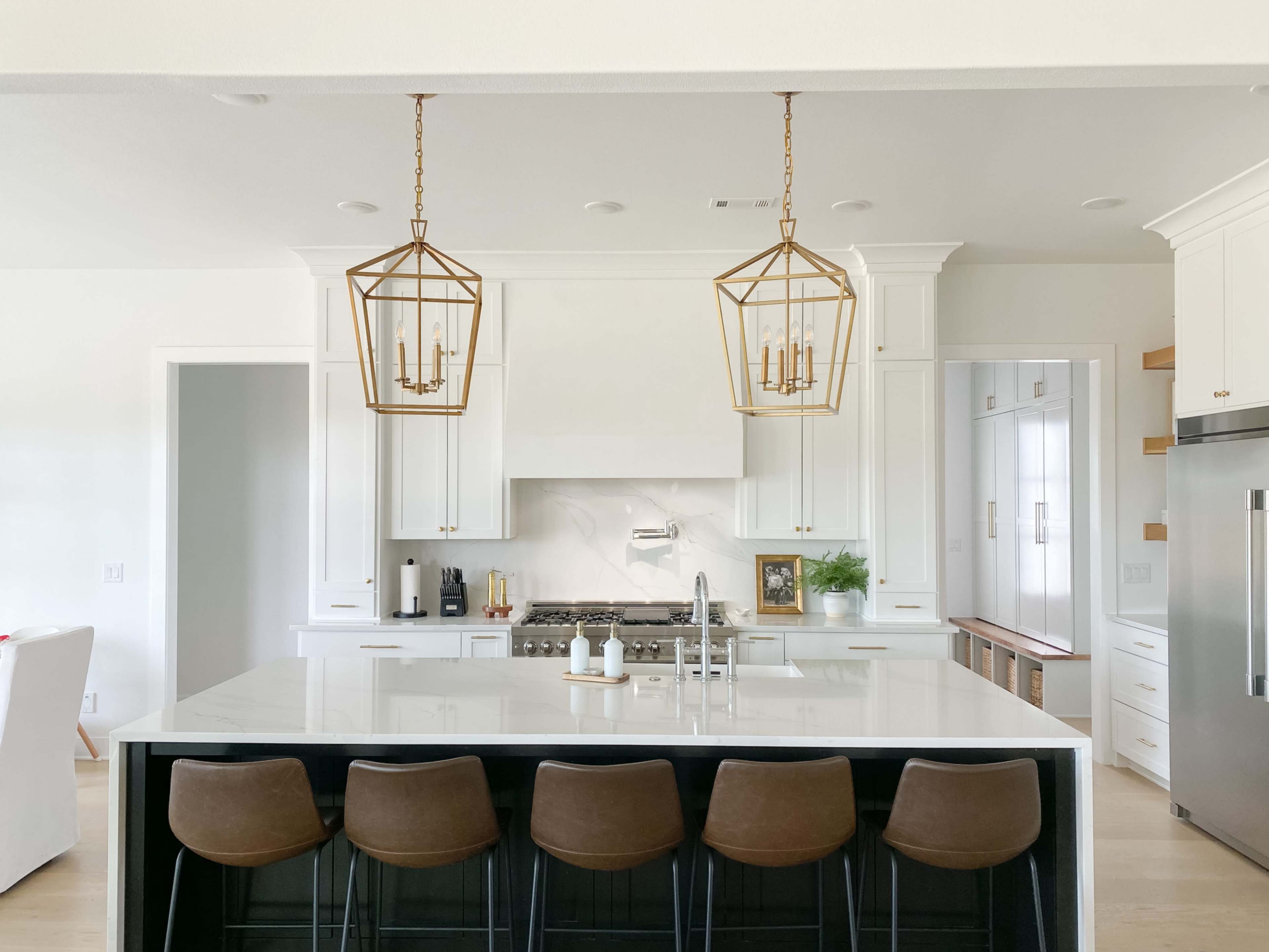 A modern kitchen with a large island, four brown bar stools, two pendant lights, and white cabinetry.