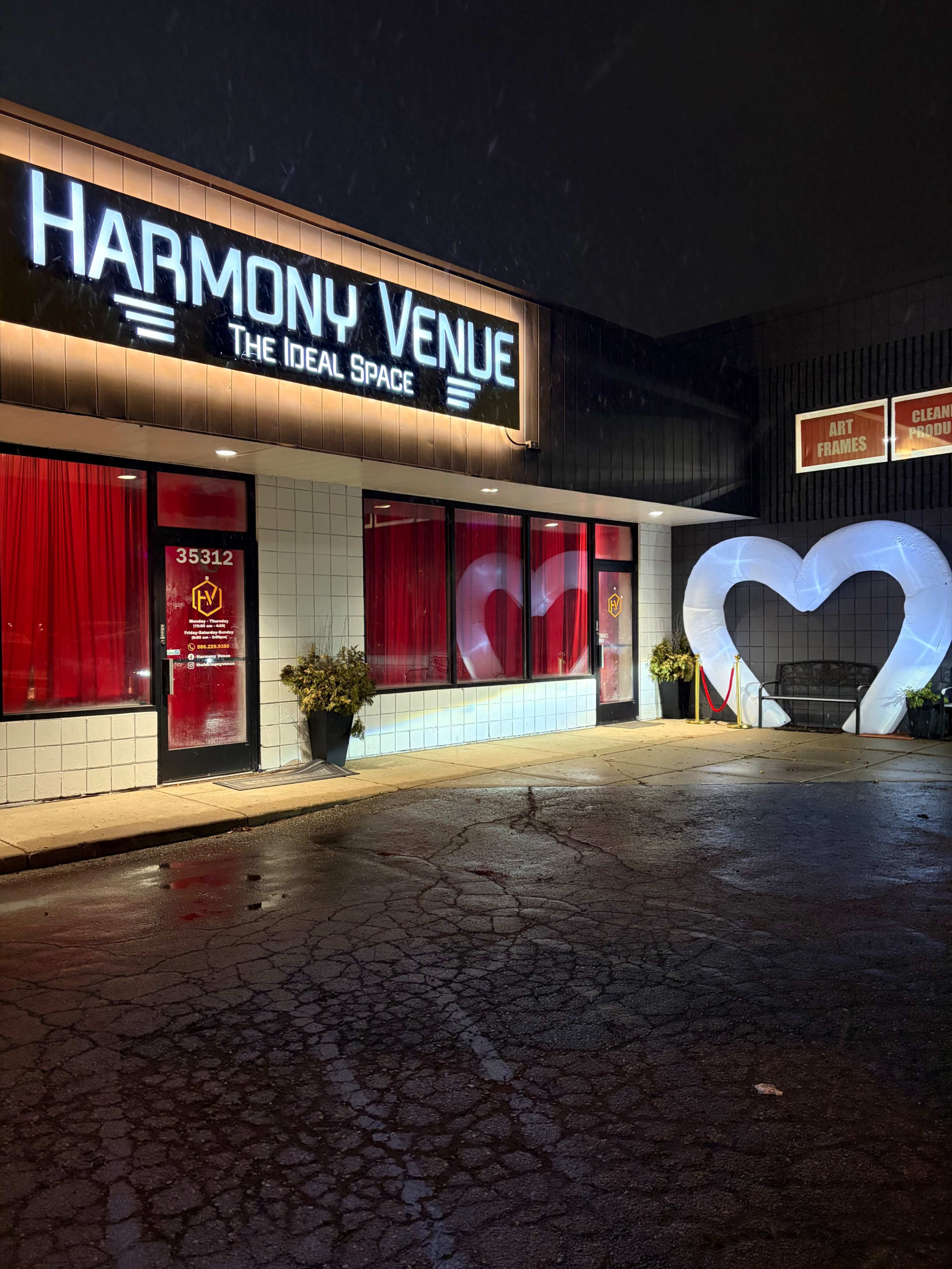 The image shows a building with a sign reading "Harmony Venue" and illuminated red curtains, featuring large heart-shaped decorations at the entrance.