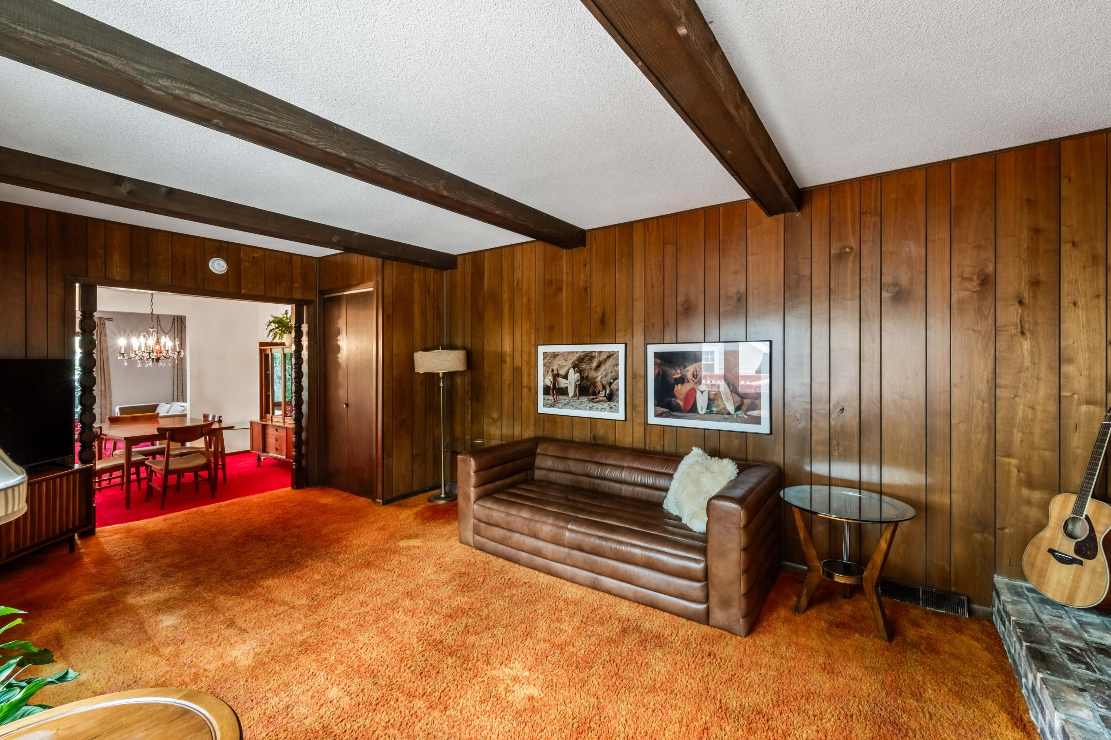 A cozy living room with wooden paneling, a brown leather sofa, and framed photographs on the walls.