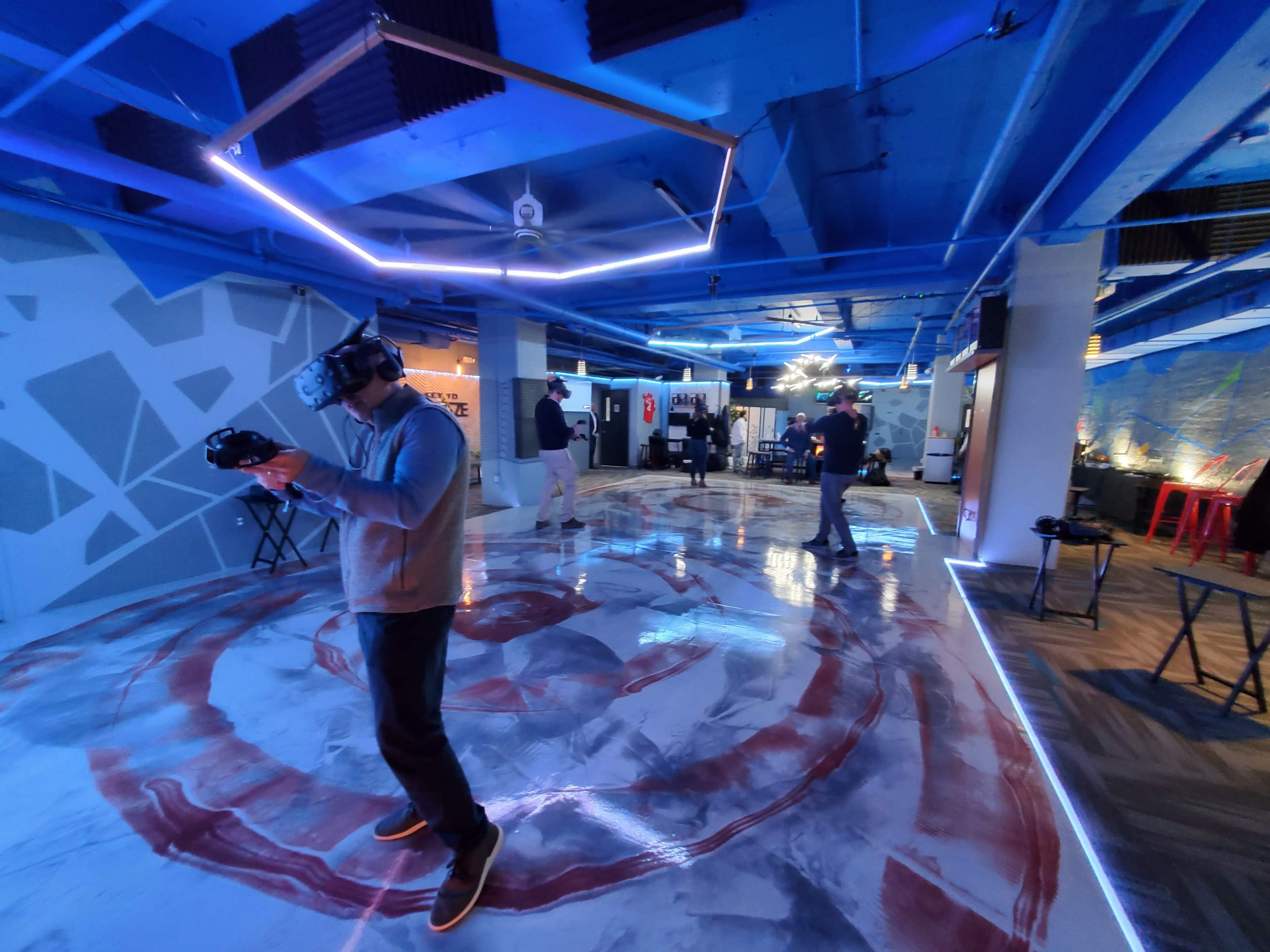 A group of people experiences virtual reality in a modern, blue-lit space with a uniquely designed floor.